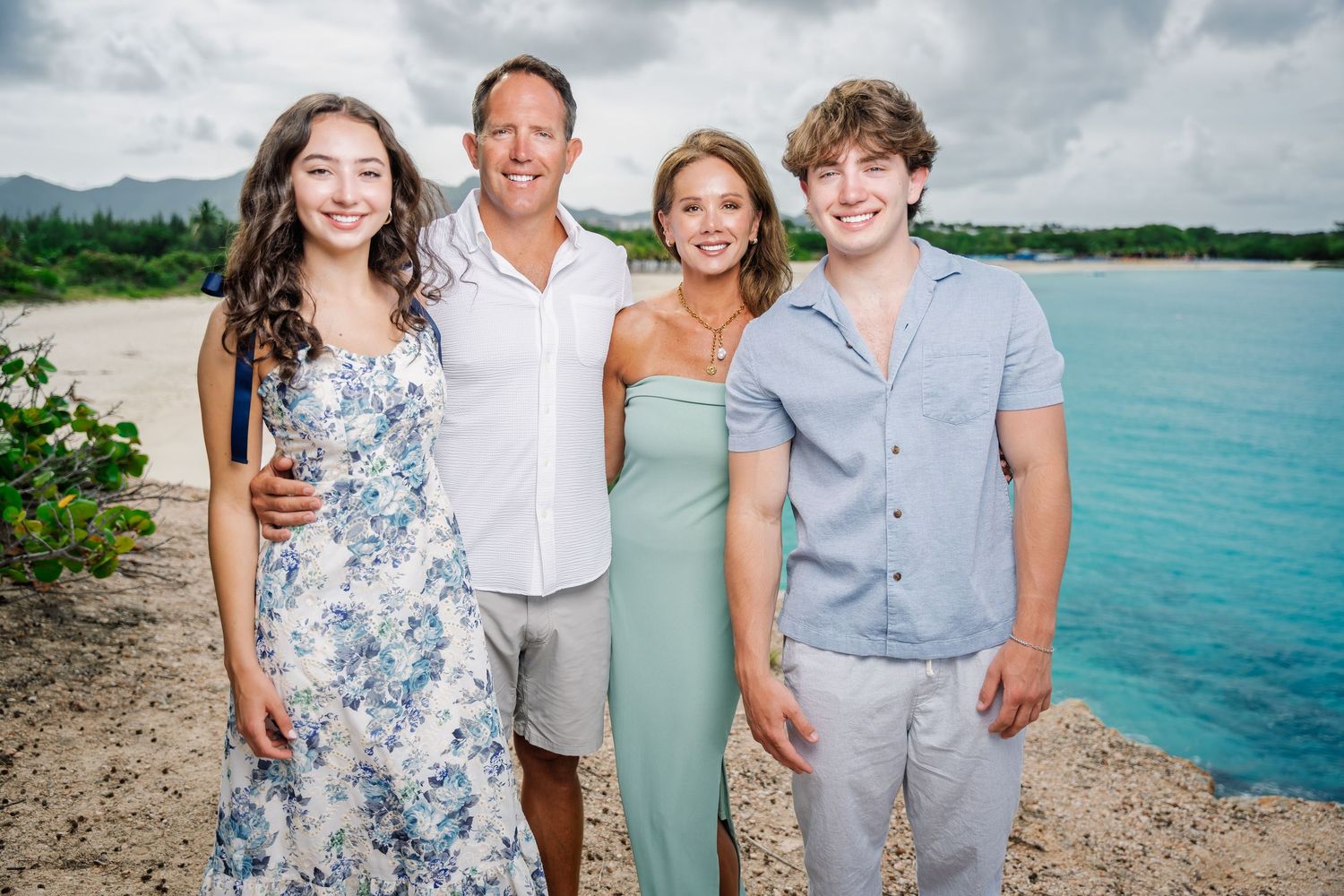 Family of four posing together on a rocky tropical beach under cloudy skies.