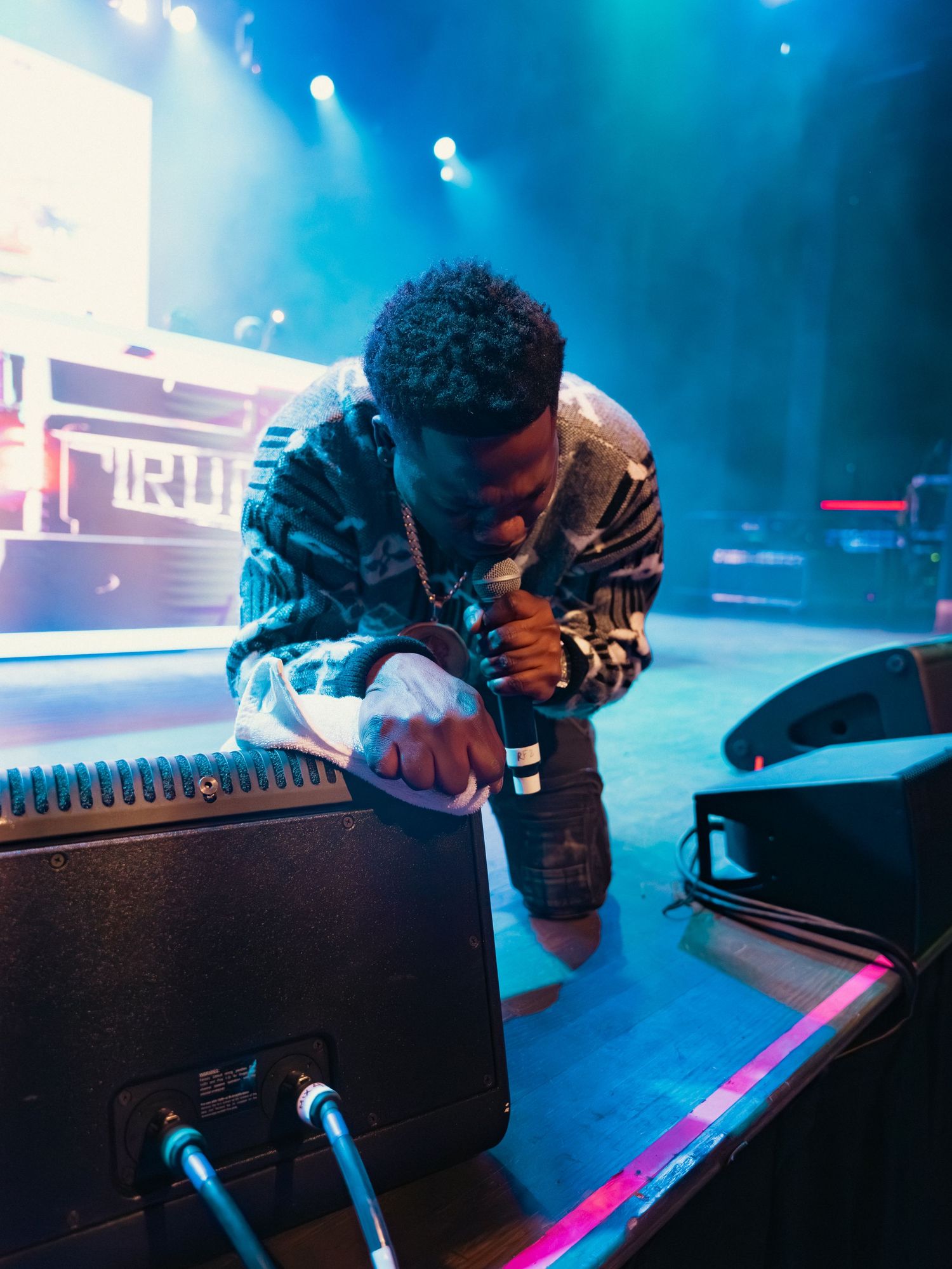 A male artist leaning toward the crowd while performing on a lit concert stage.