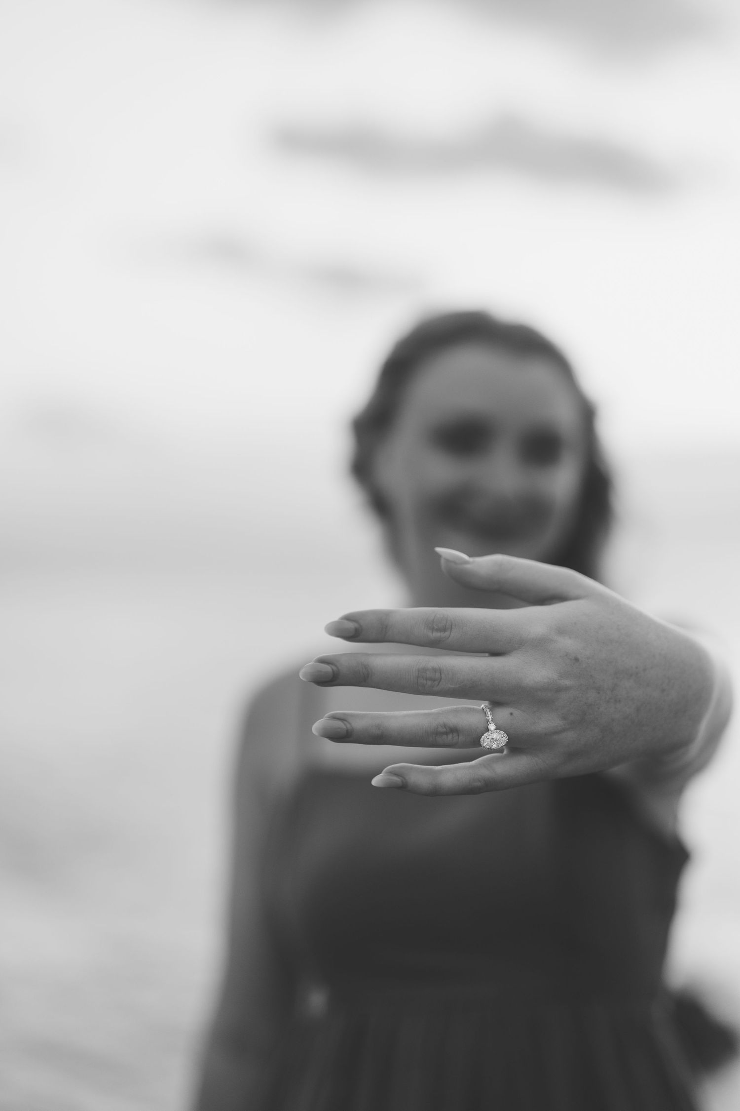 Black and white photo of smiling bride showing off her diamond engagement ring to camera.