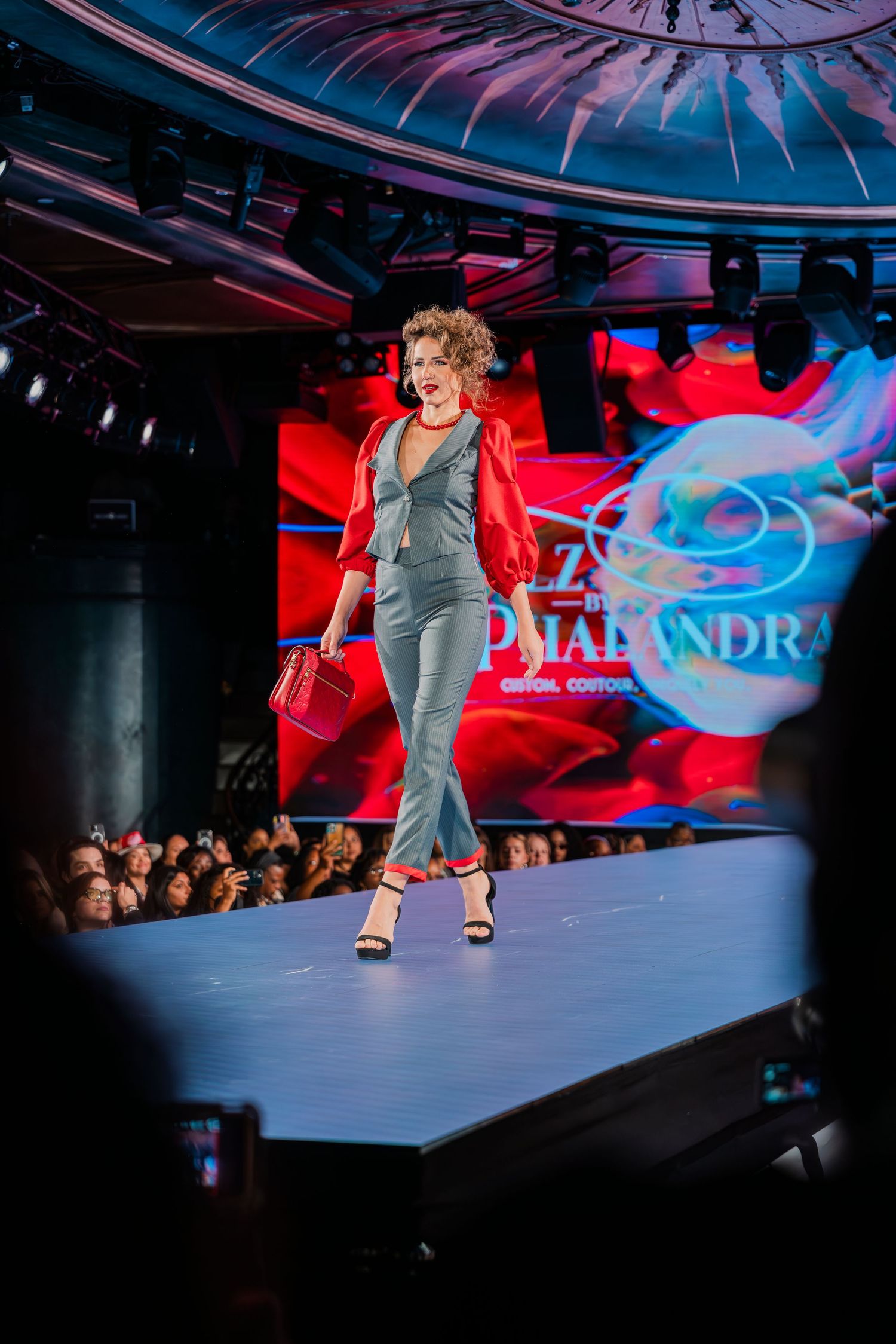 A model walks the runway in a gray jumpsuit and red jacket at a Z by Pmarandra fashion show.