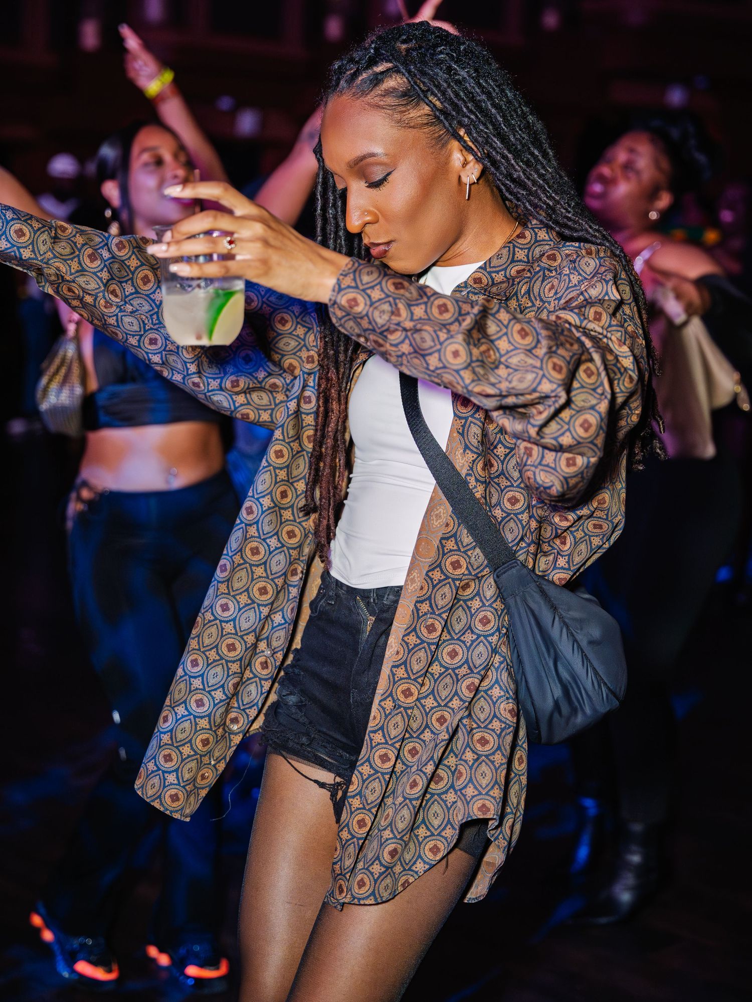 Woman in patterned jacket dances expressively at an energetic nighttime party.