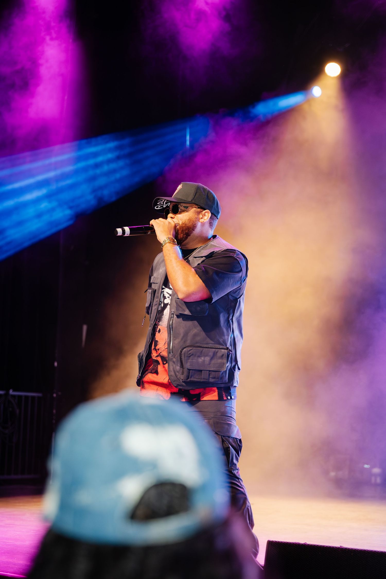 A soca artist performs on a smoke-filled stage under colorful purple and yellow spotlights.