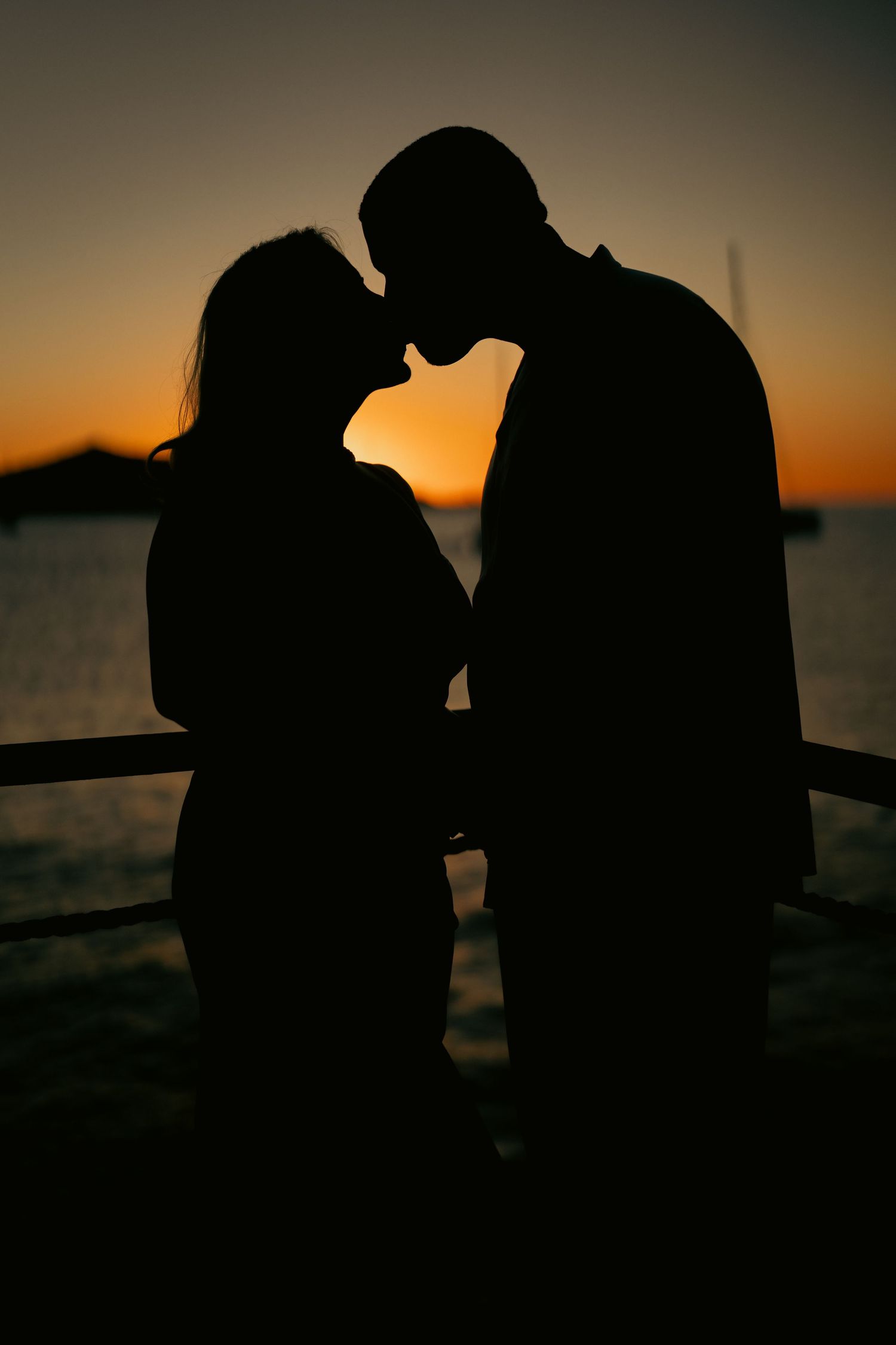 Romantic silhouette of couple sharing a kiss at sunset by the waterfront.