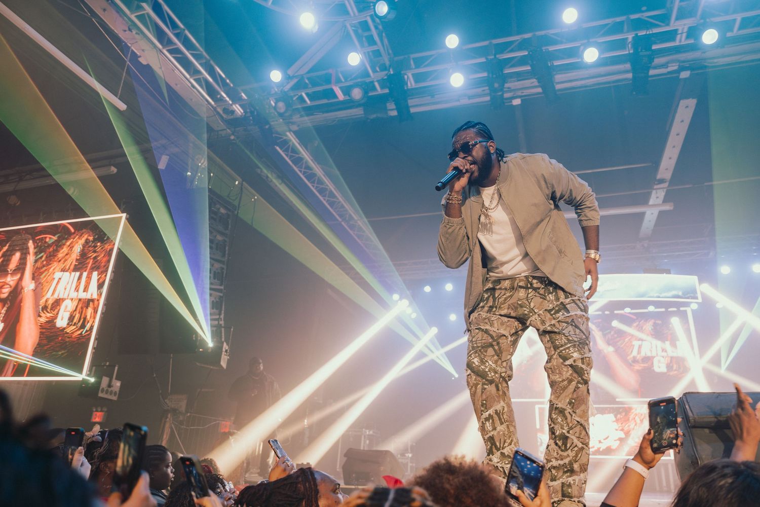 Rapper performing on stage above crowd with colorful stage lighting at concert.