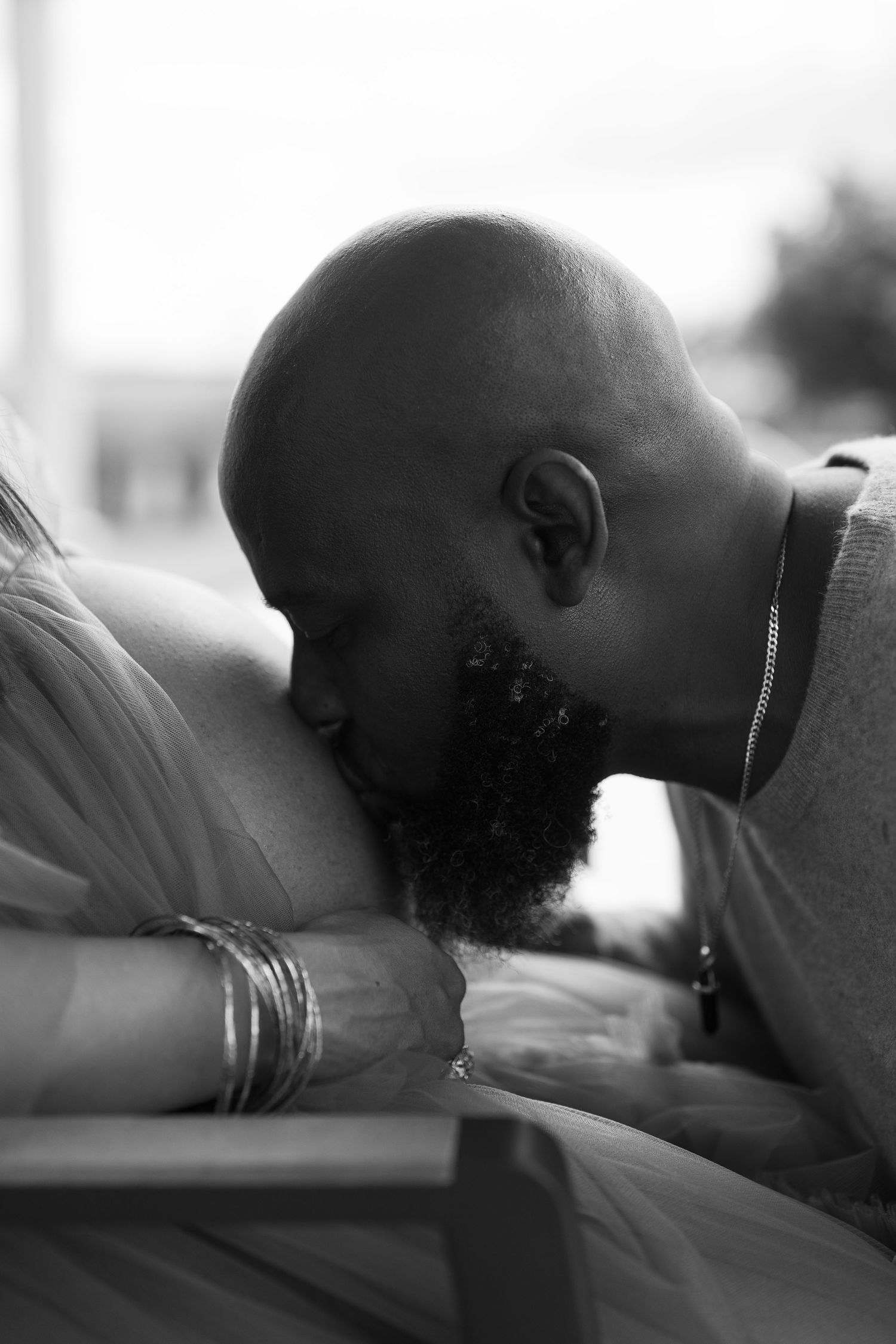 Black and white photo of a bald bearded man tenderly kissing a pregnant woman's baby bump.
