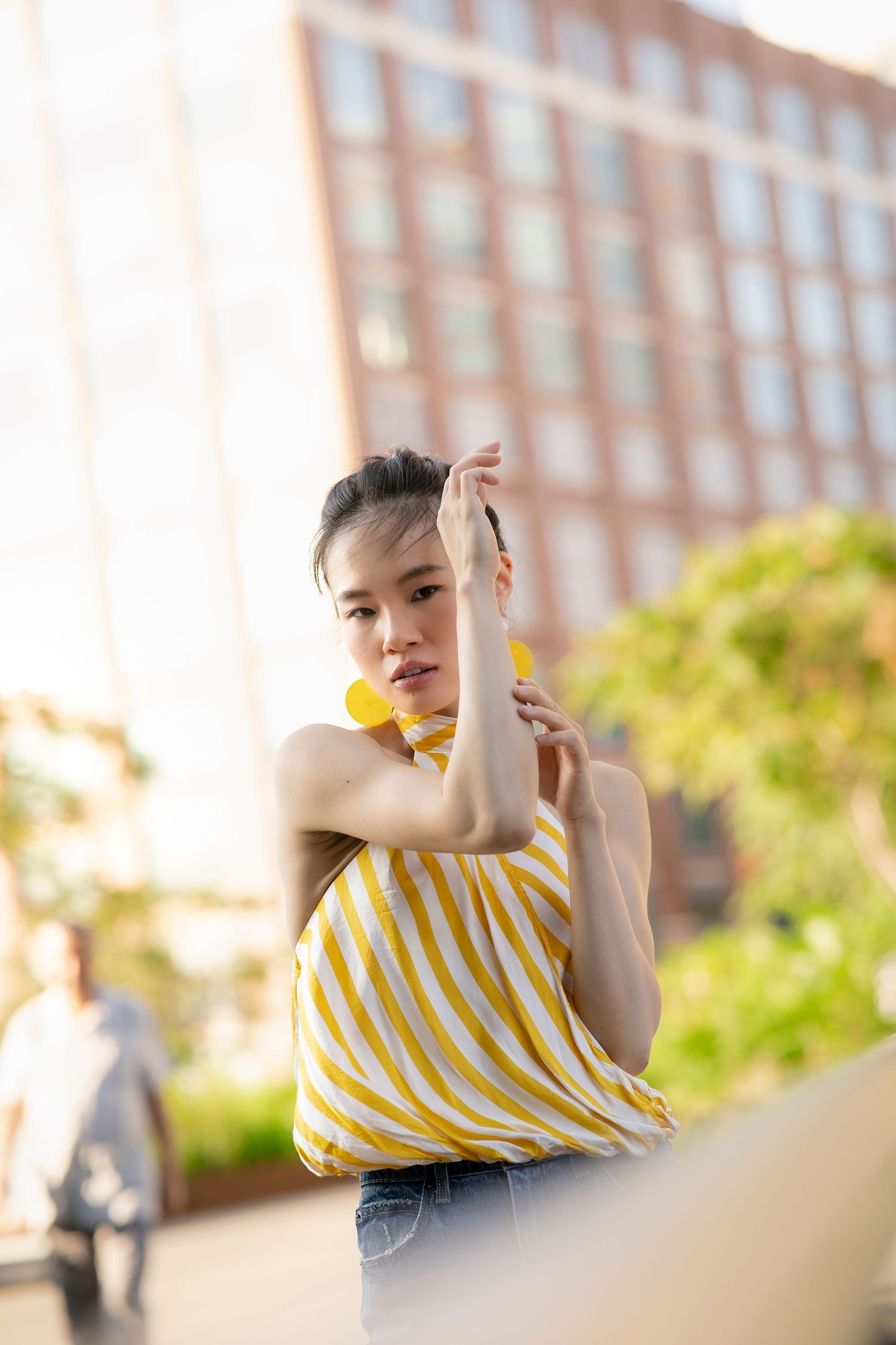 Young Asian woman in yellow striped strapless top with matching earrings posing in urban setting.