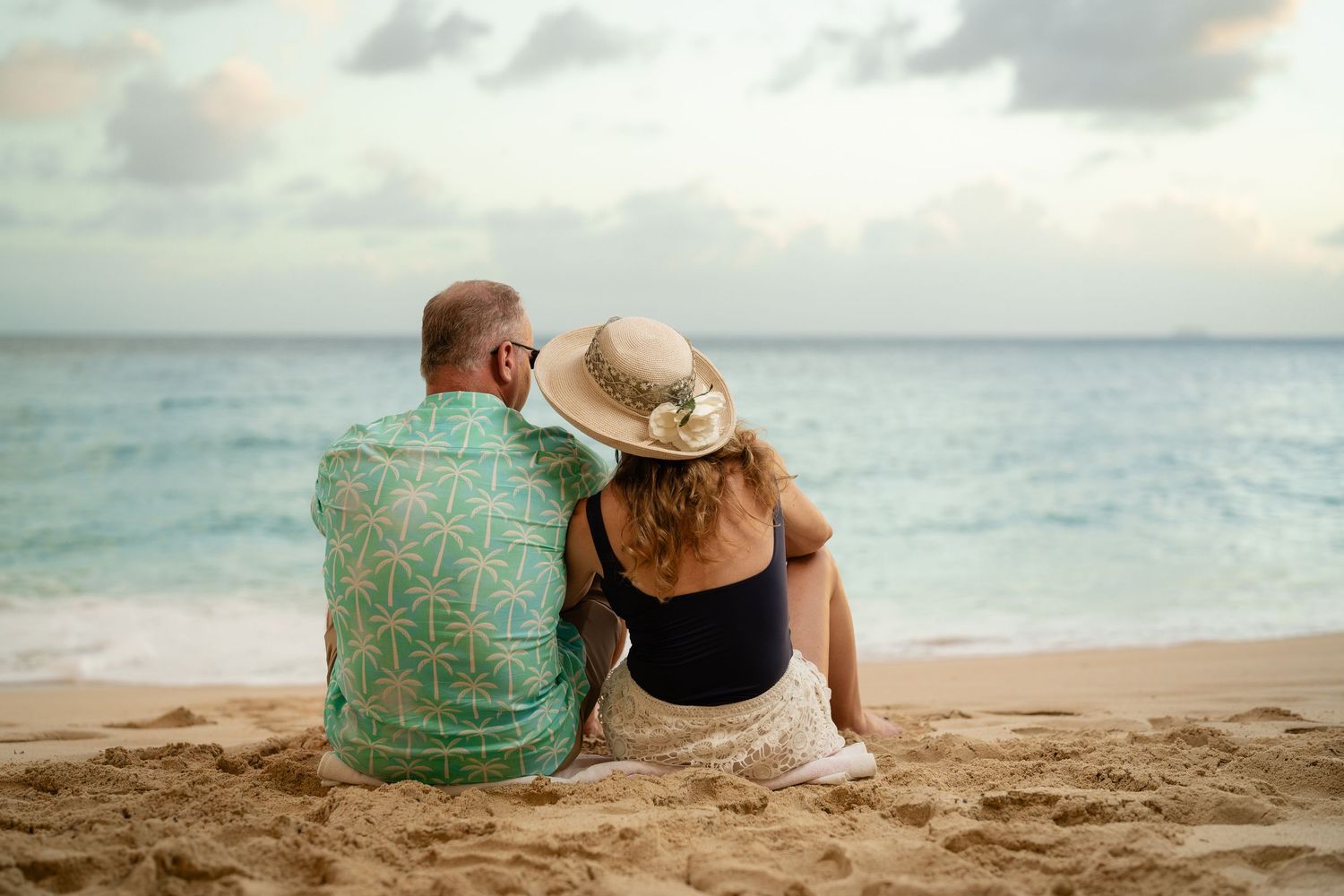 Couple sitting together on sandy beach gazing at ocean waves during golden hour.