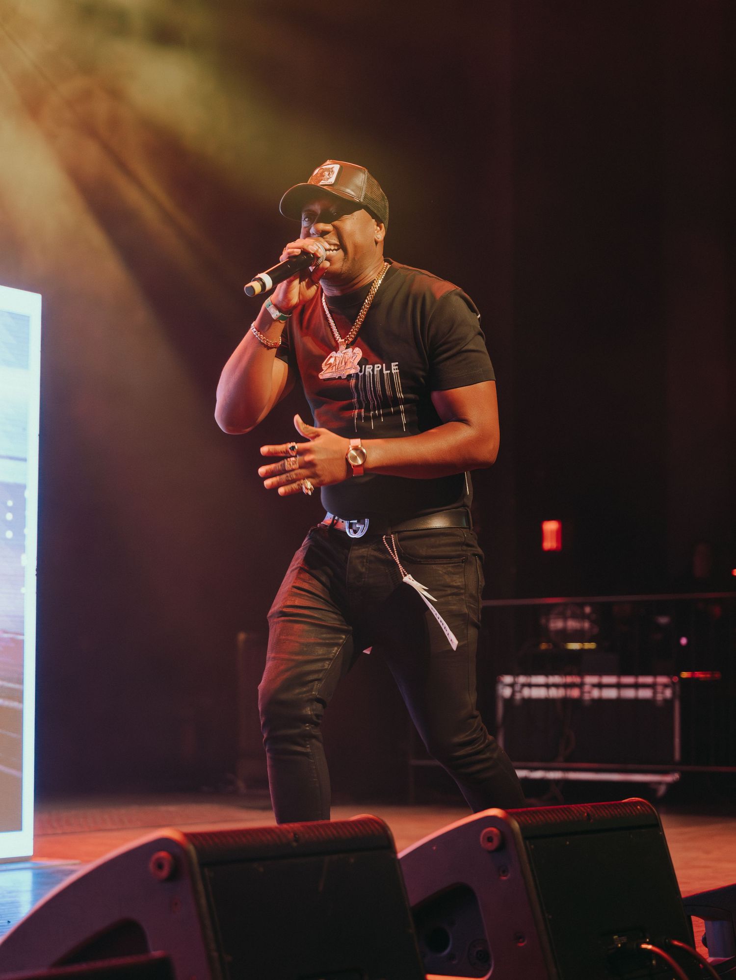 Male soca artist performs on stage holding microphone under warm golden stage lighting.