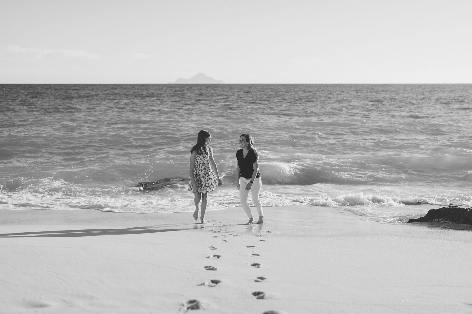 Black and white photo of two people facing each other on a beach with footprints in the sand.