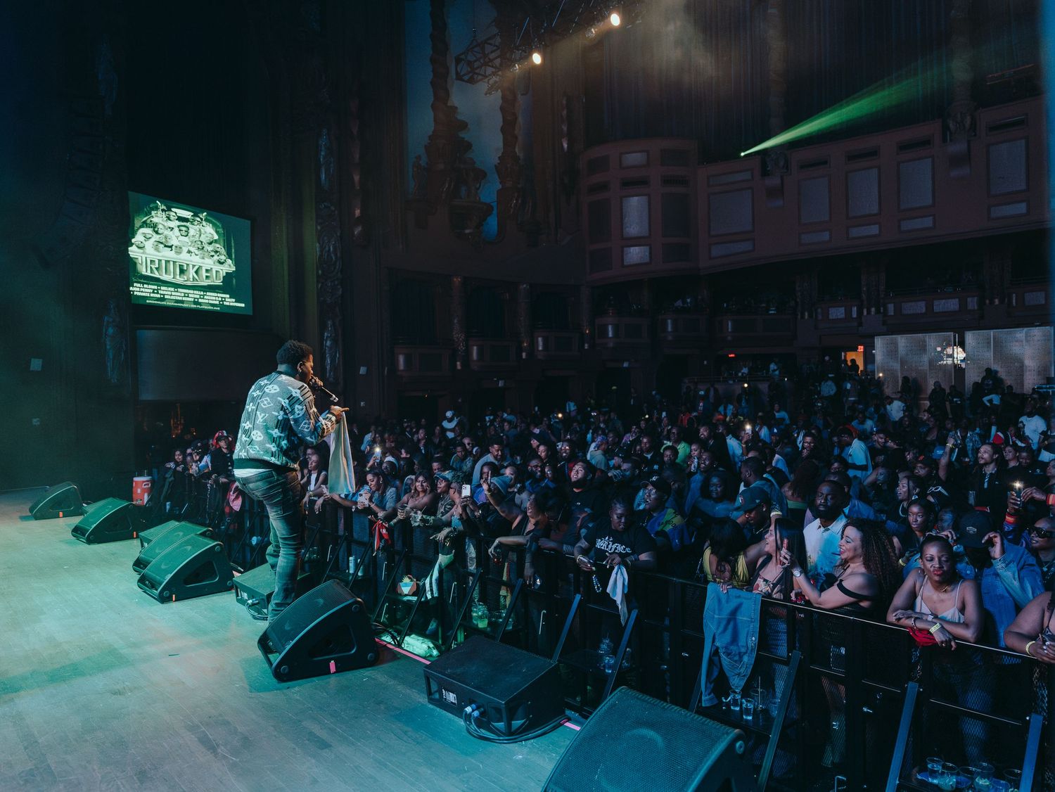 A performer on stage facing a large energetic crowd at an indoor concert.