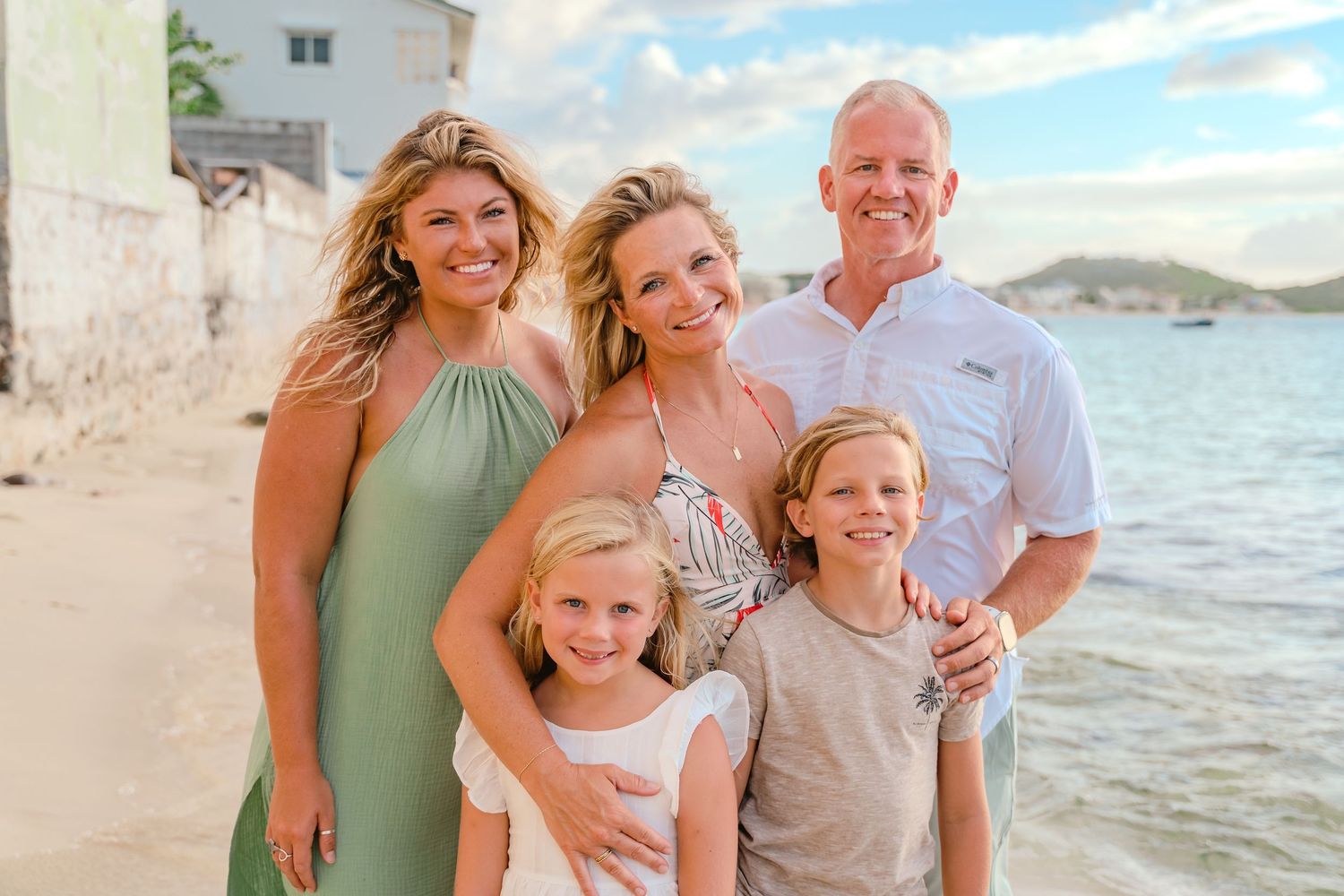 Family of five smiling together on a tropical beach at golden hour.