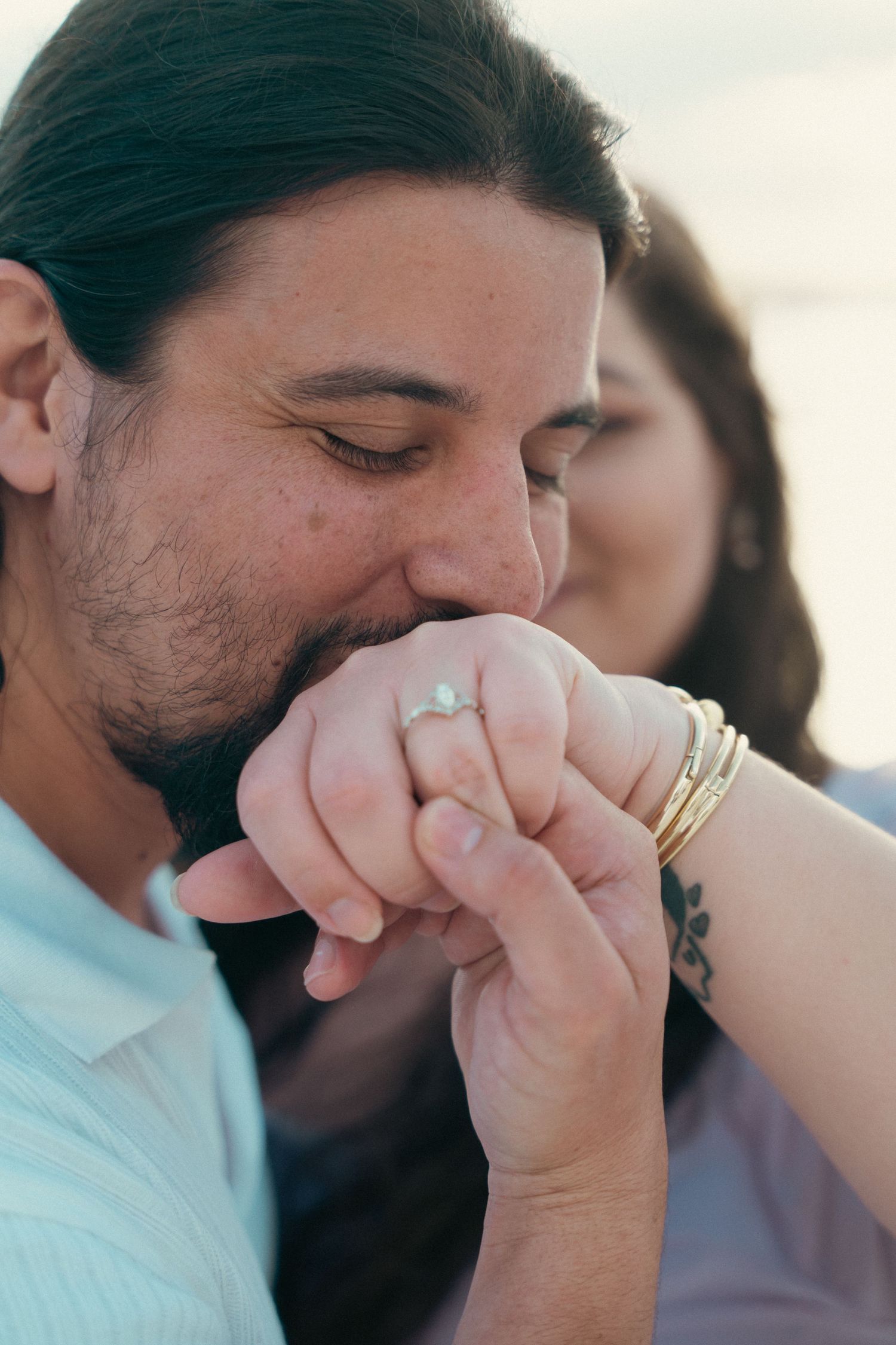 Man kissing woman's hand adorned with pearl ring and gold bangles in romantic gesture.