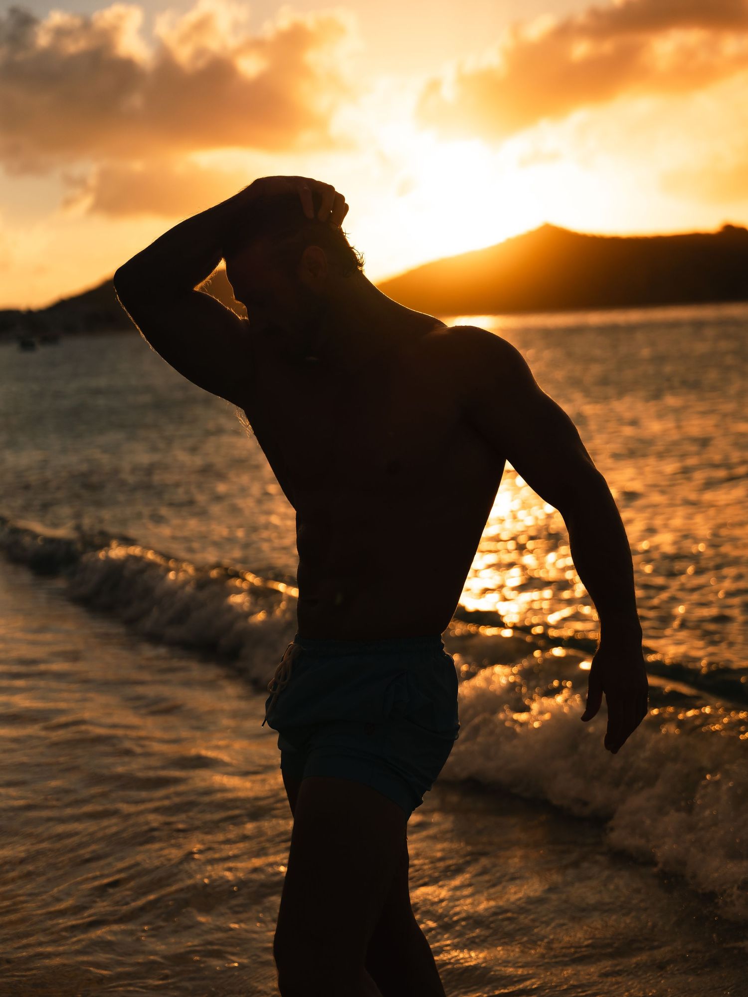 Silhouette of muscular man standing on beach shoreline during vibrant golden sunset.