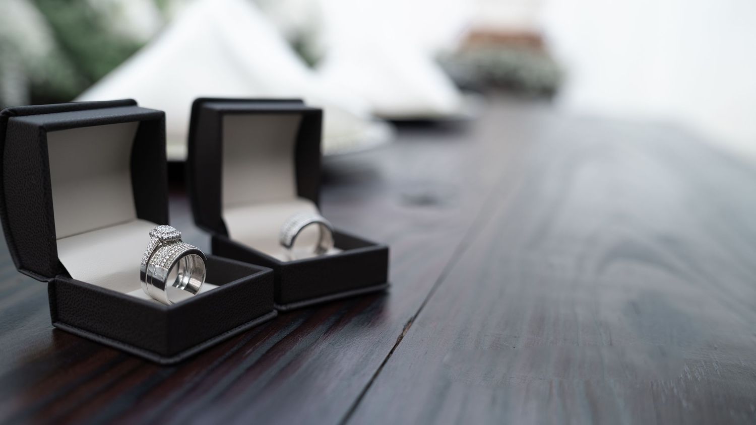 Two wedding rings displayed in black velvet boxes on a wooden table.