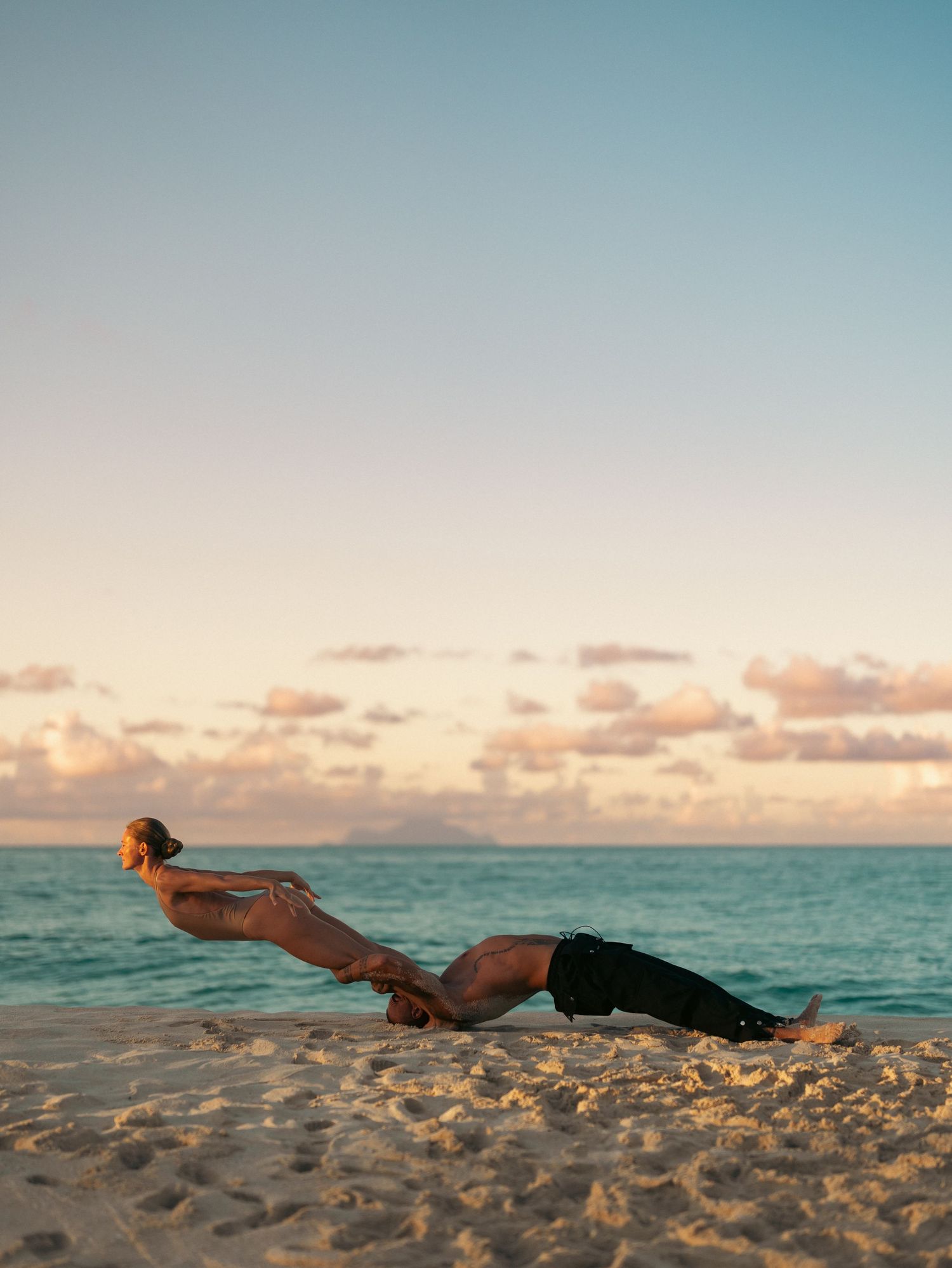 Couple performing acrobatic beach yoga pose at sunset on a tropical sandy shore.