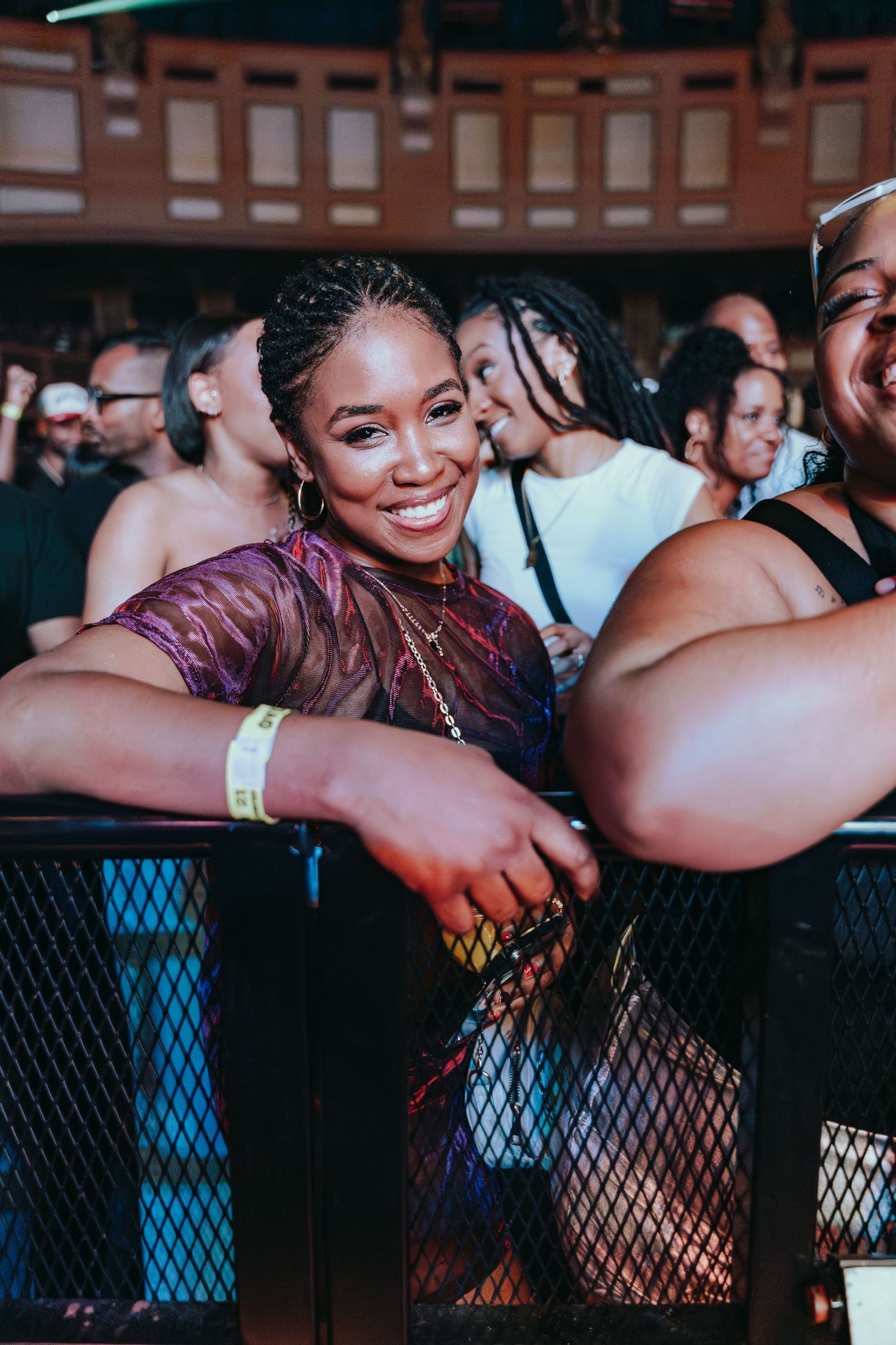 A smiling woman leaning on a barrier at a live music concert.