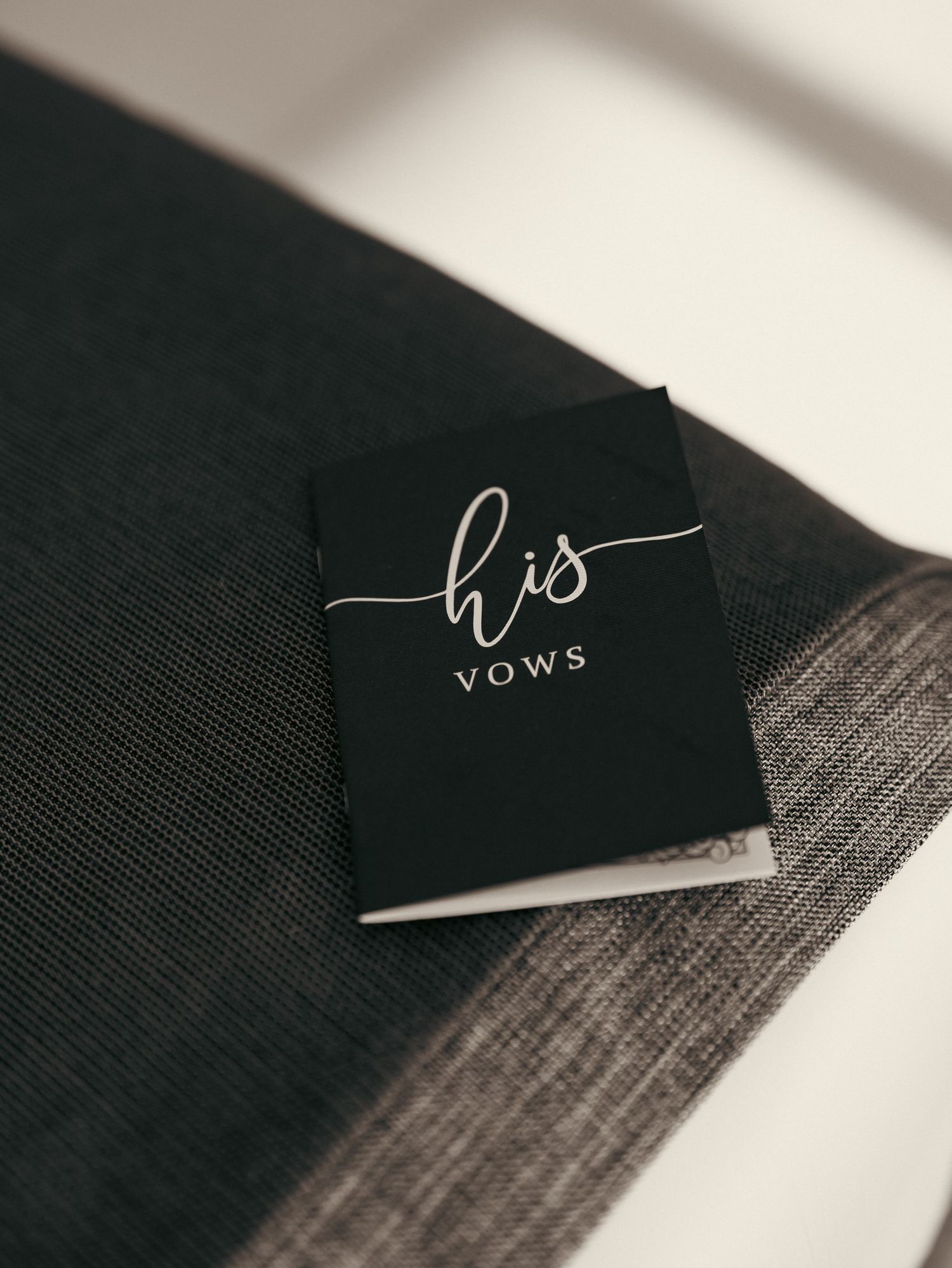 Black wedding vow booklet with silver script reading his vows placed on a dark gray textured surface.