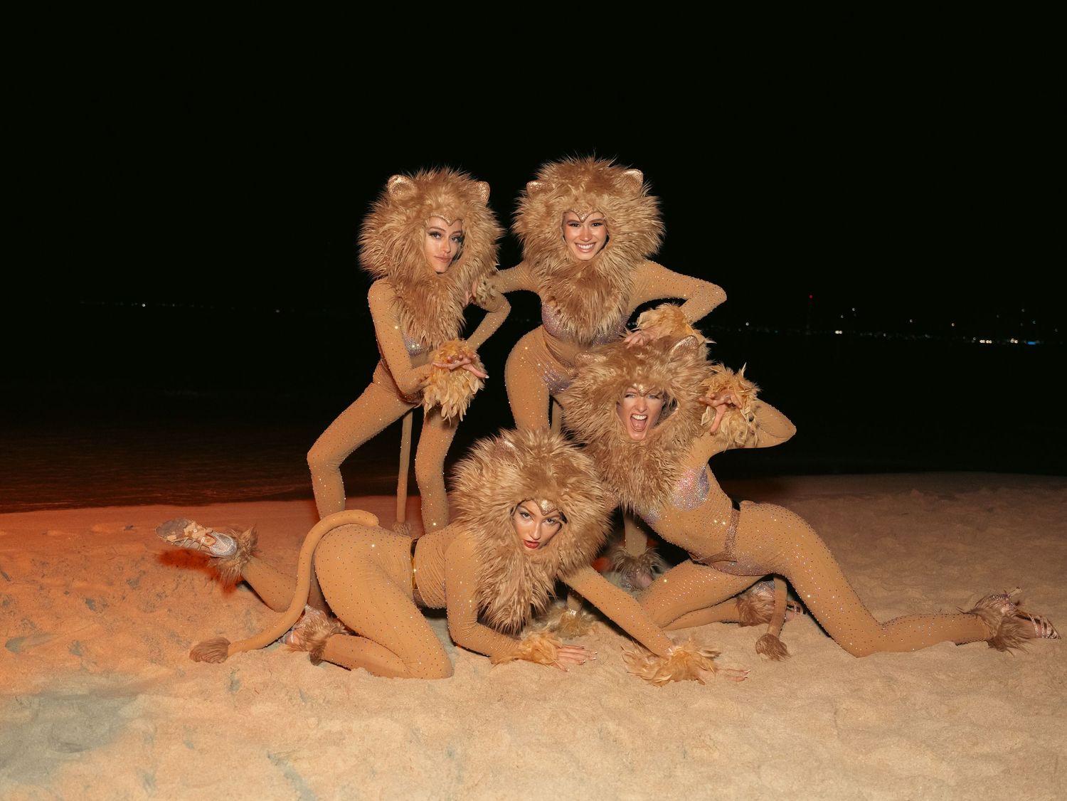 Four performers in lion costumes posing together on a sandy surface at night.