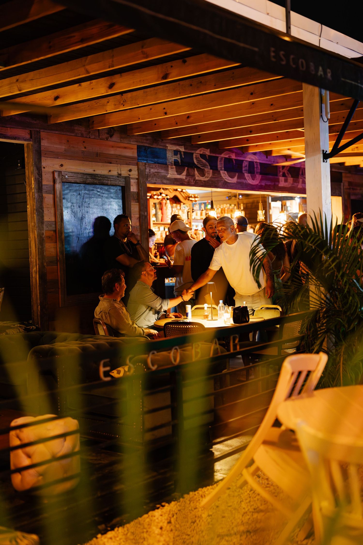 Guests socializing at Escobar bar at night with warm lighting and tropical decor.