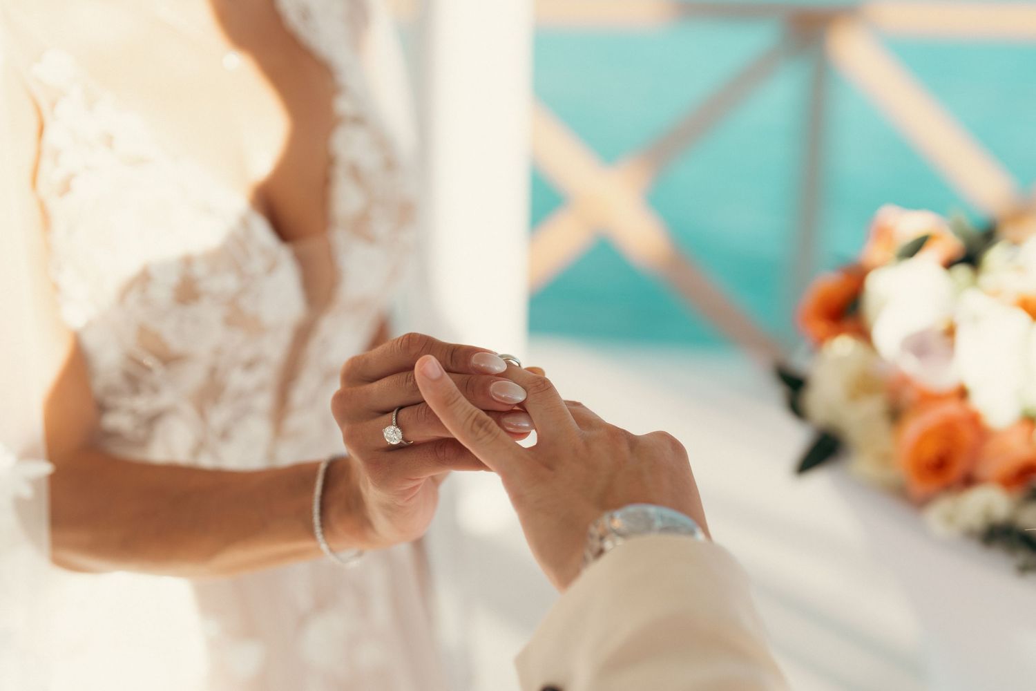 Close-up of couple exchanging wedding rings during beach ceremony with floral arrangement.