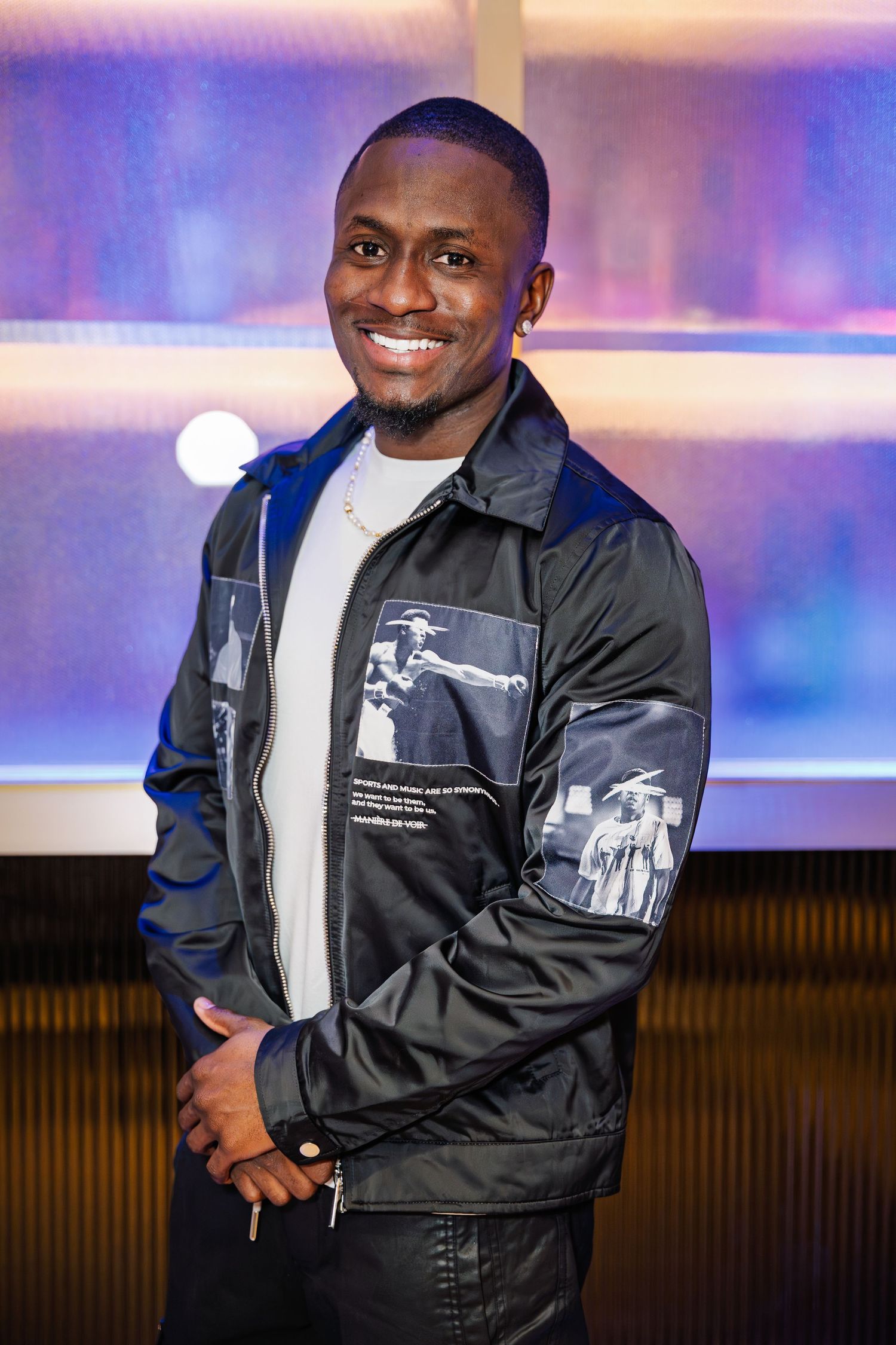 Smiling young man in graphic jacket poses at a vibrant nightlife venue.