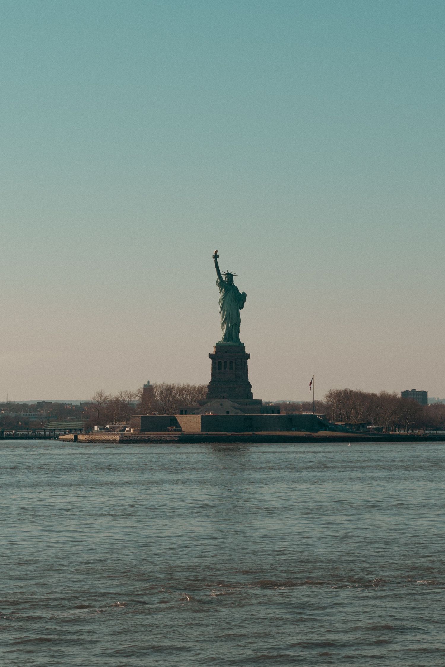 Statue of Liberty standing tall on Liberty Island viewed from the water at dusk.