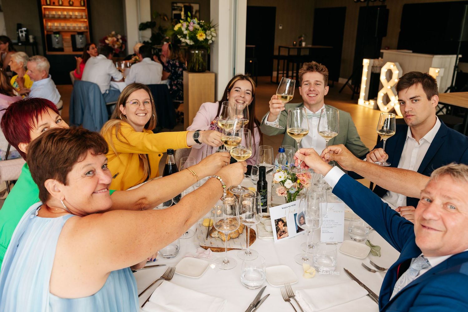 Happy wedding guests raise champagne glasses in celebratory toast at elegantly decorated reception table.