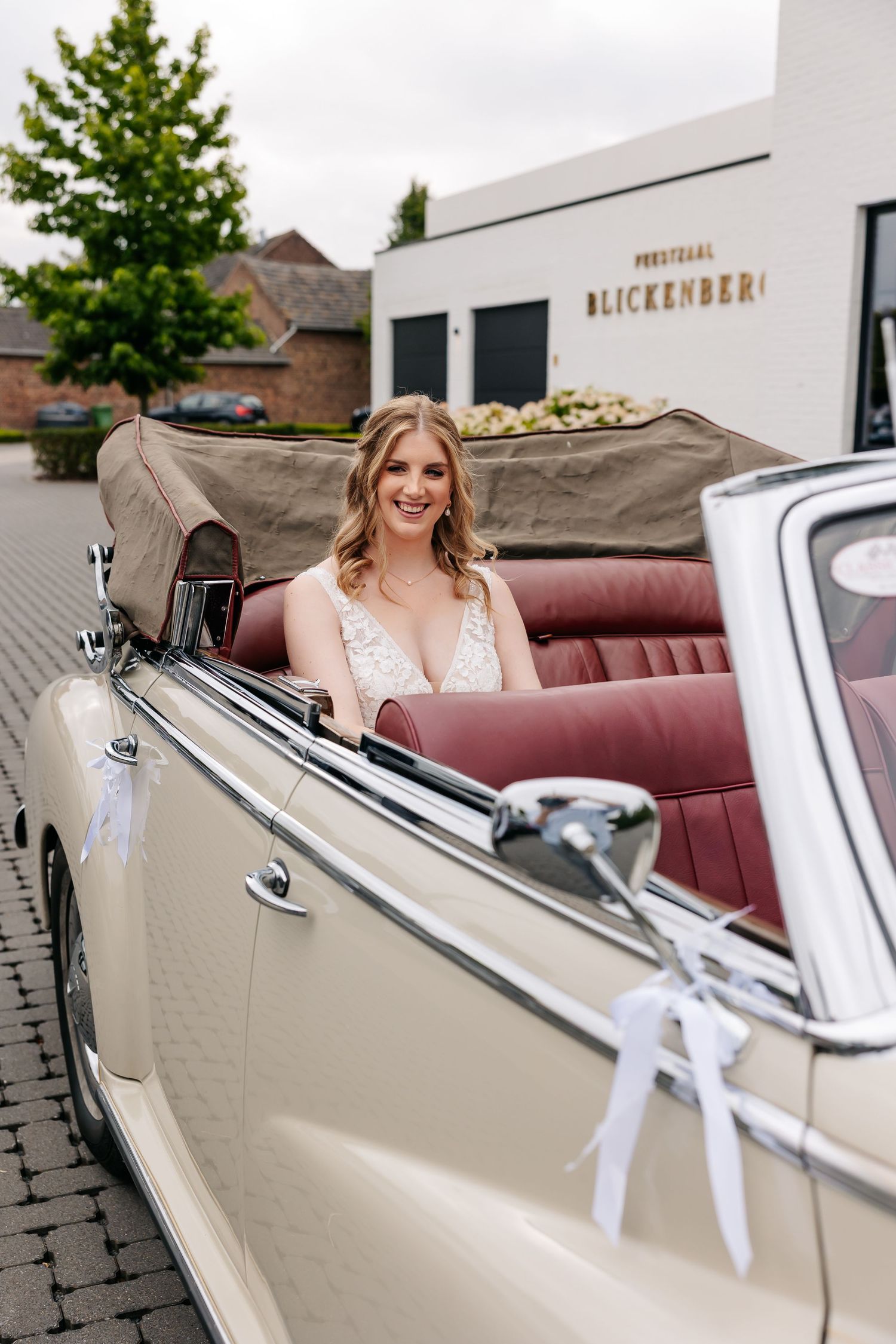 Radiant bride seated in vintage cream Mercedes convertible with red interior outside Blickenberg wedding venue.