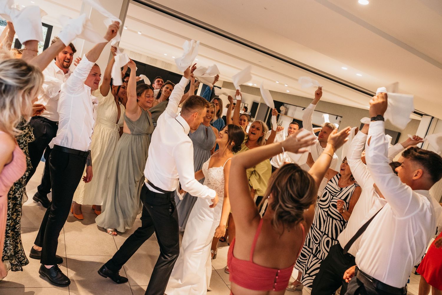 Energetic wedding reception crowd waving napkins and dancing together.