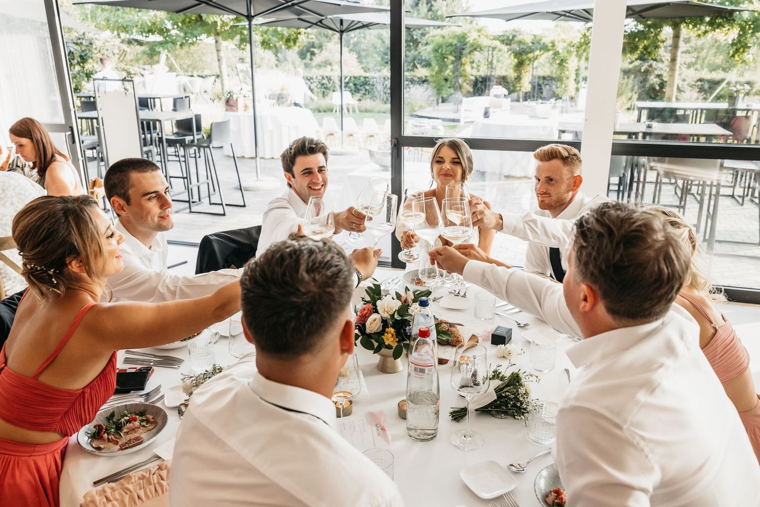 Wedding party guests raising champagne glasses in a toast at a floral-decorated reception table.