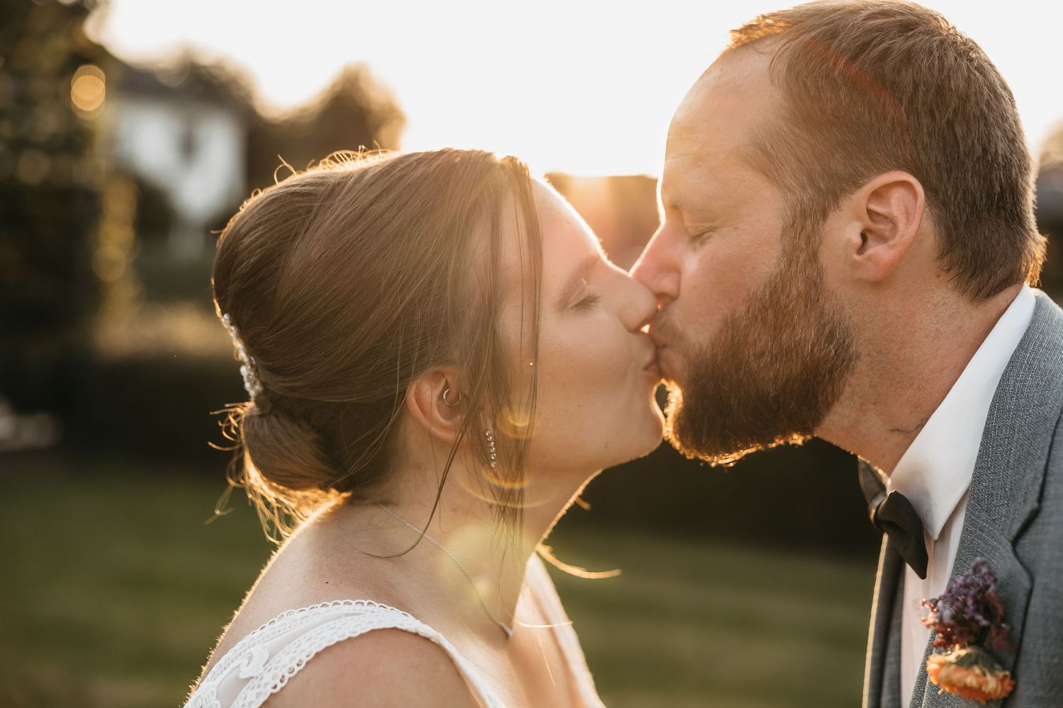 Newlyweds sharing a tender kiss outdoors with beautiful golden sunset bokeh background.