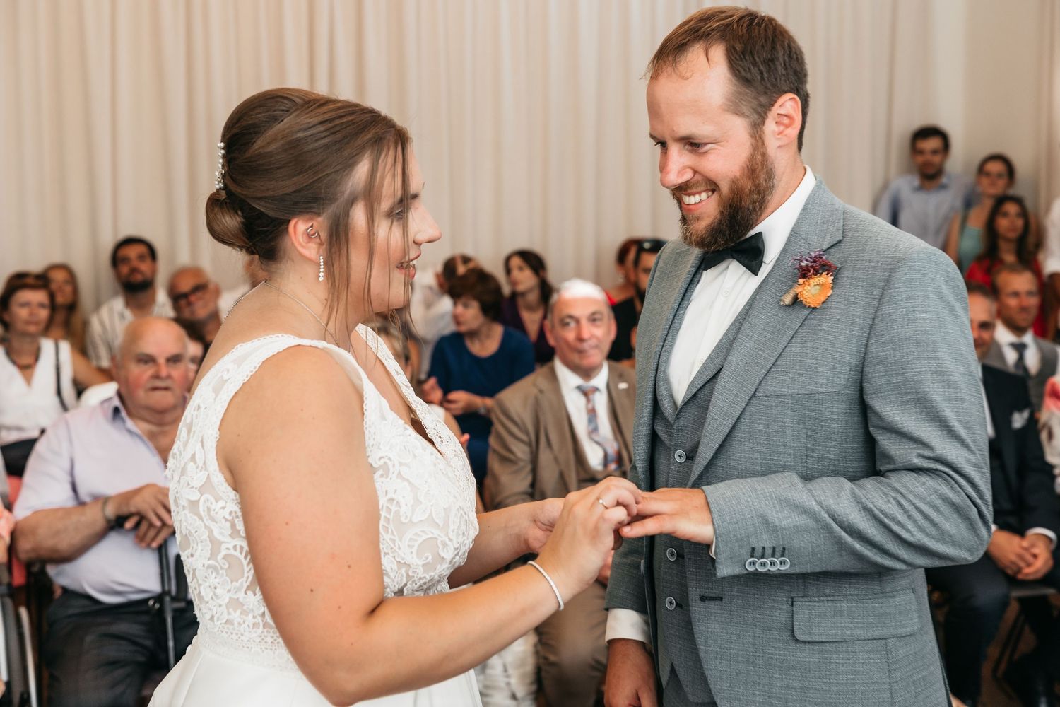 Bride smiles while placing a wedding ring on the grooms finger during the ring exchange ceremony.
