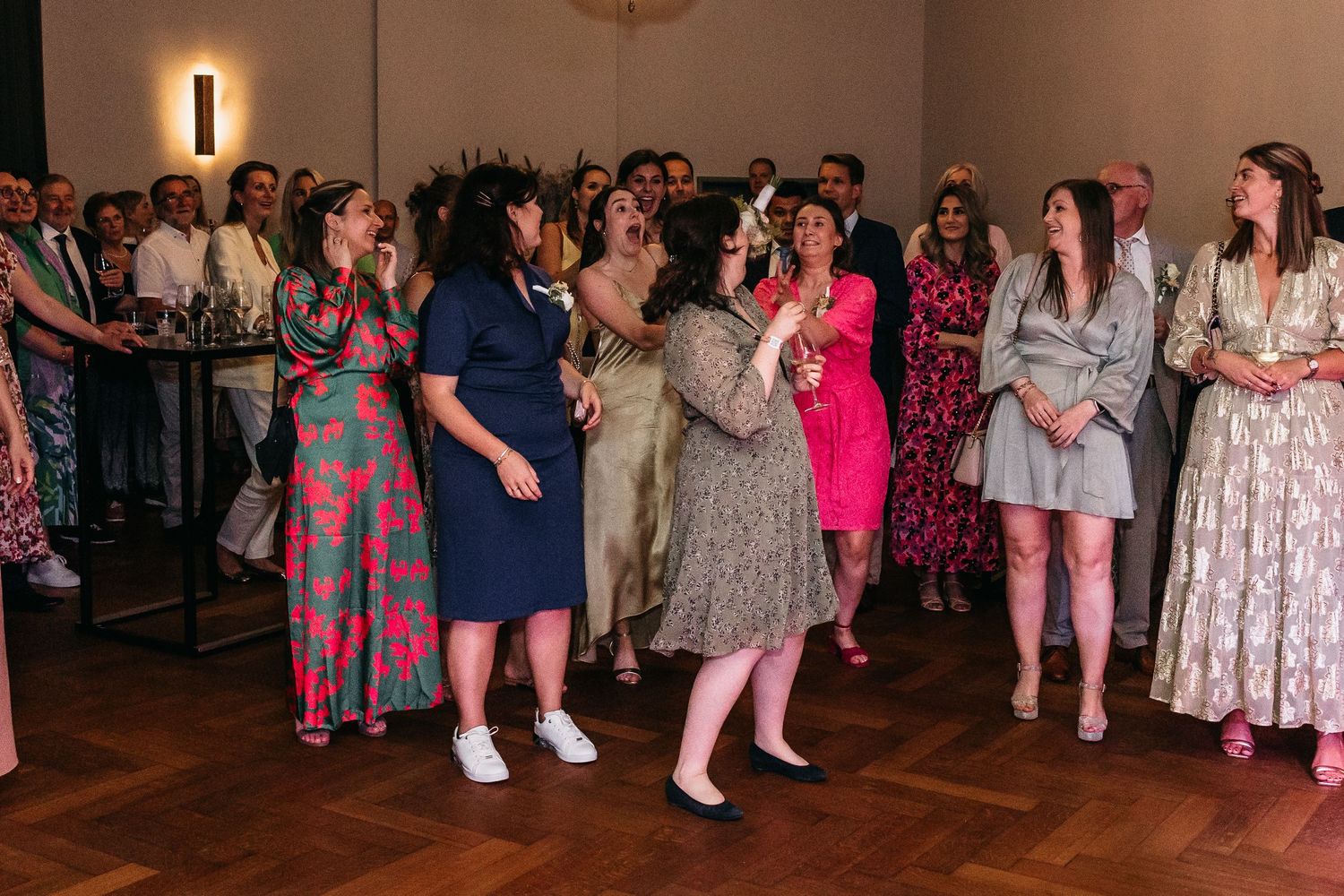 Excited wedding guests reach out to catch bridal bouquet toss at indoor reception.