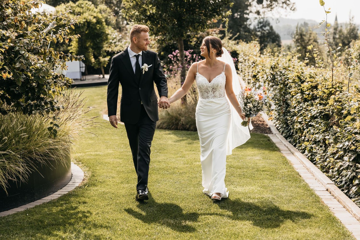 Bride and groom stroll hand in hand along a lush garden path on their wedding day.