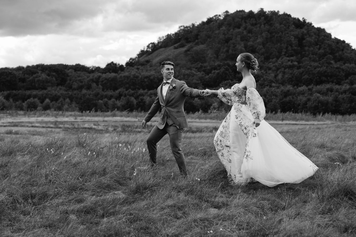 Black and white photo of bride and groom holding hands in open field.