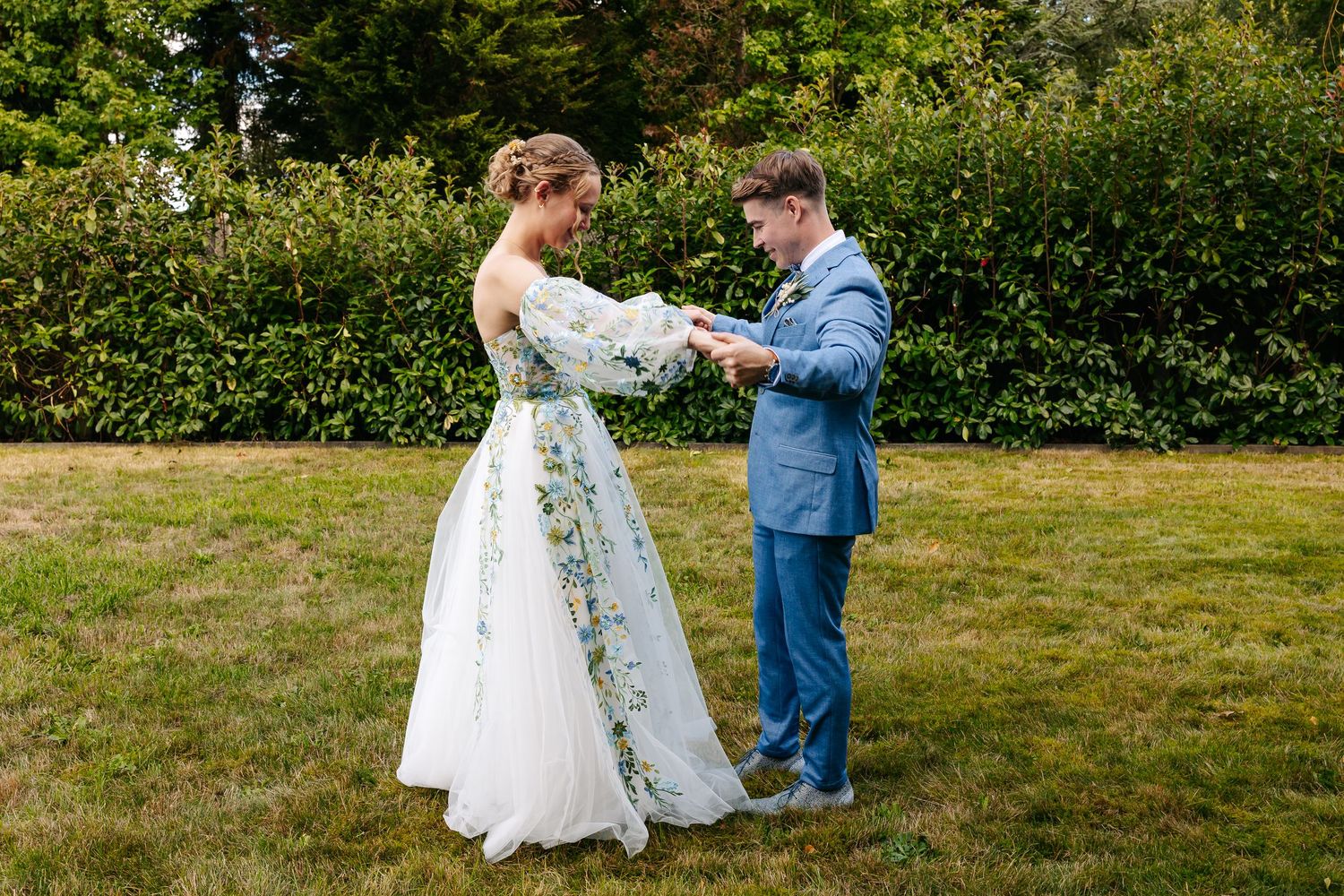 Bride reads vows from paper while groom listens attentively during outdoor garden wedding ceremony.