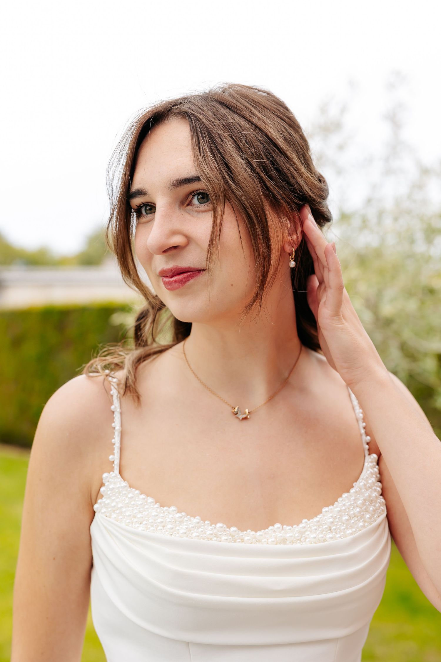 Beautiful brunette bride in pearl-trimmed white gown posing in a garden setting.