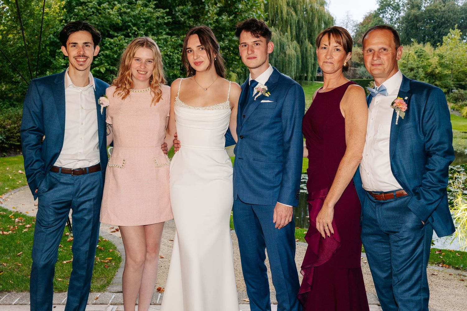 Wedding party family portrait with bride in white gown and guests in blue and burgundy attire.