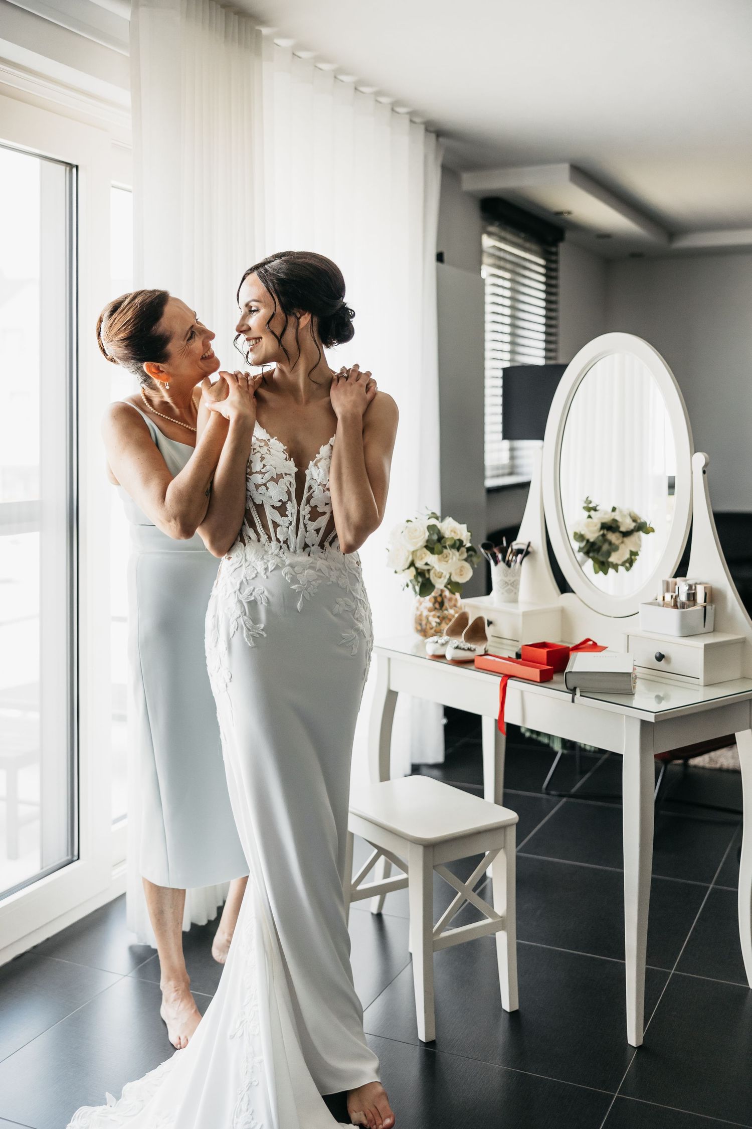 Mother and bride sharing a joyful moment after putting on wedding dress.