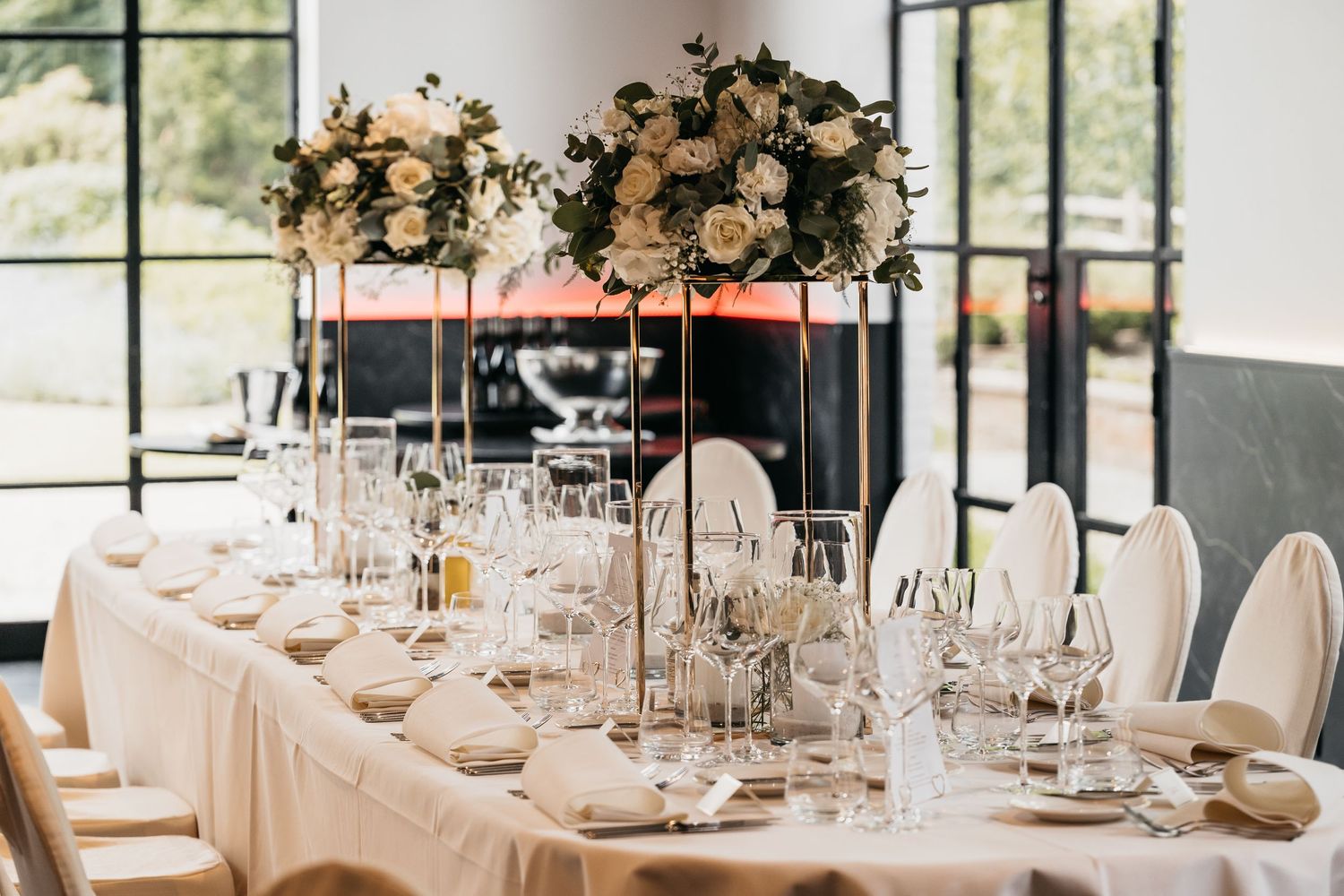 Elegant wedding head table with tall white floral centerpieces, crystal glassware, and garden views.