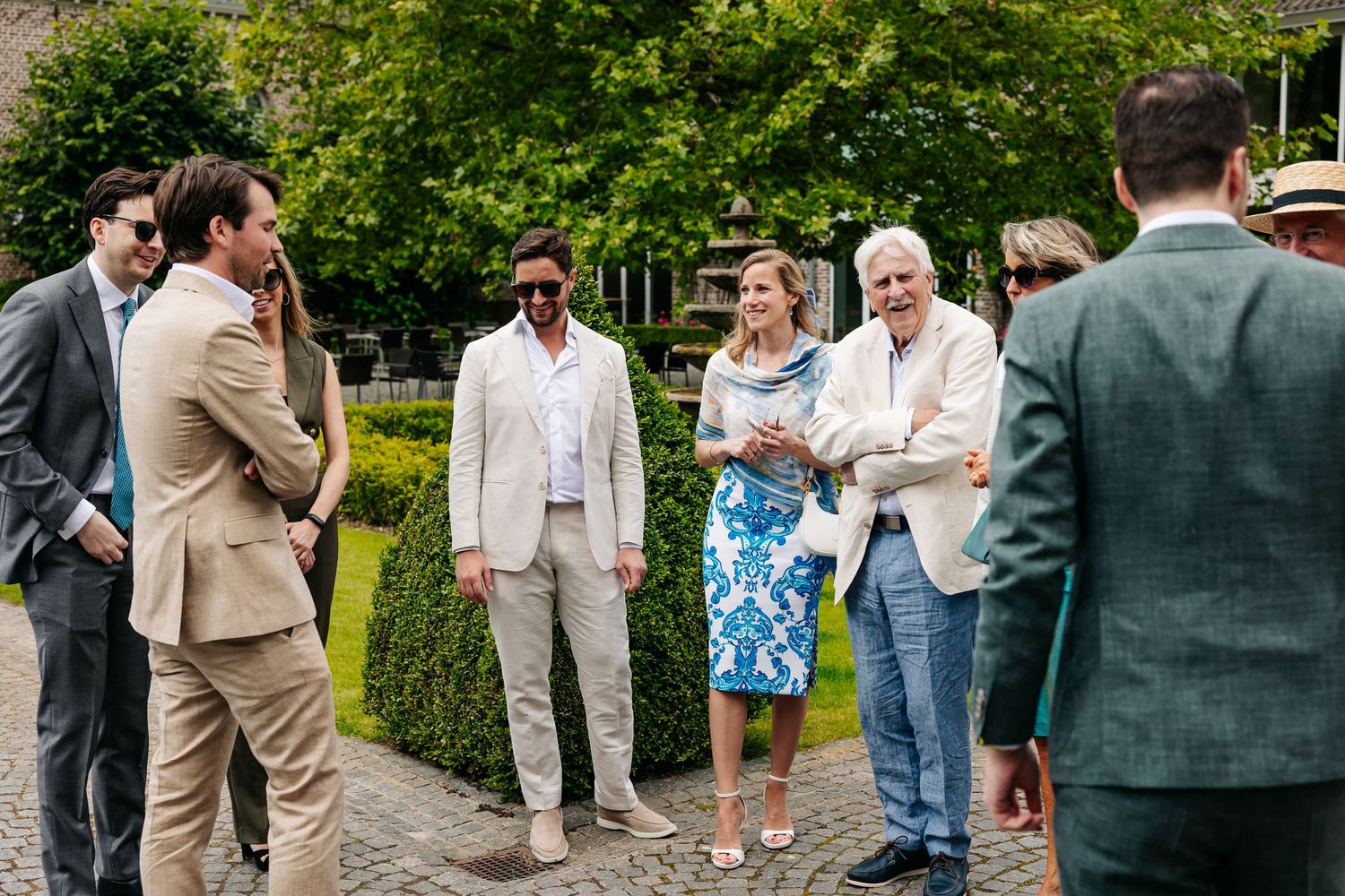 Smartly dressed wedding guests mingling in sunny garden at outdoor wedding reception.