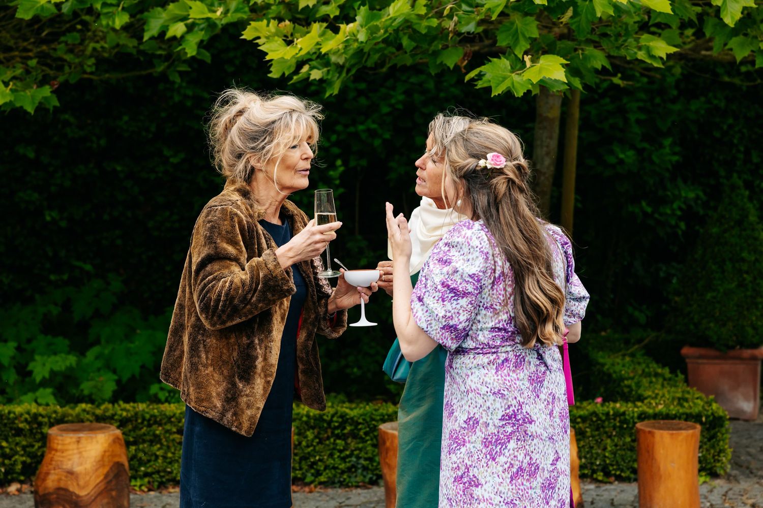 Three women socializing outdoors at a wedding reception, holding champagne glasses.