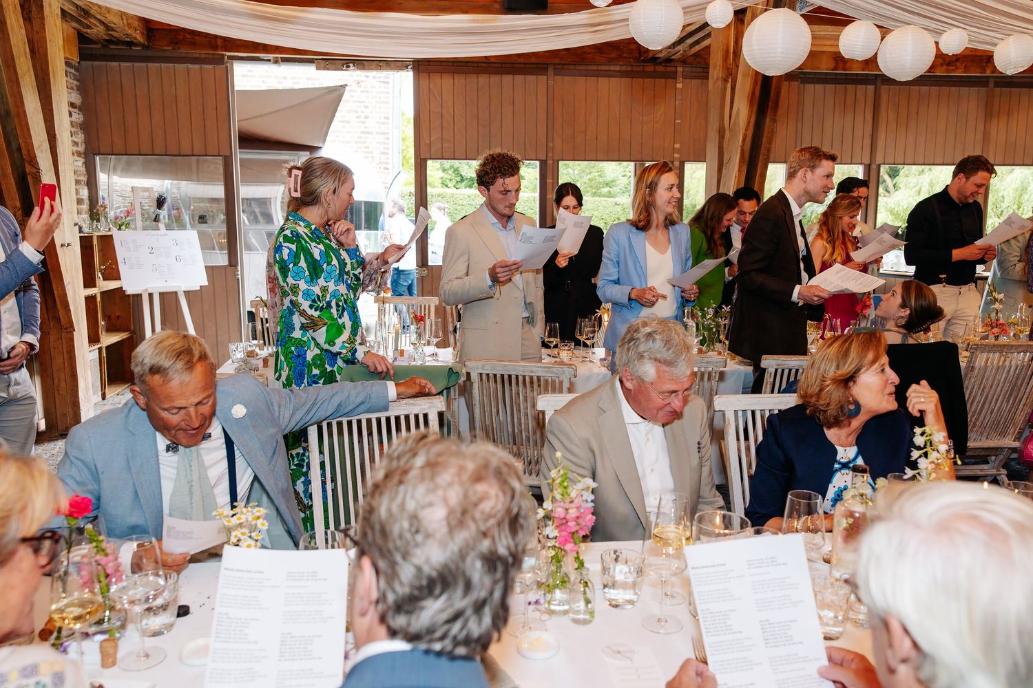 Wedding reception guests mingling and dining in an elegant outdoor pavilion with floral centerpieces.