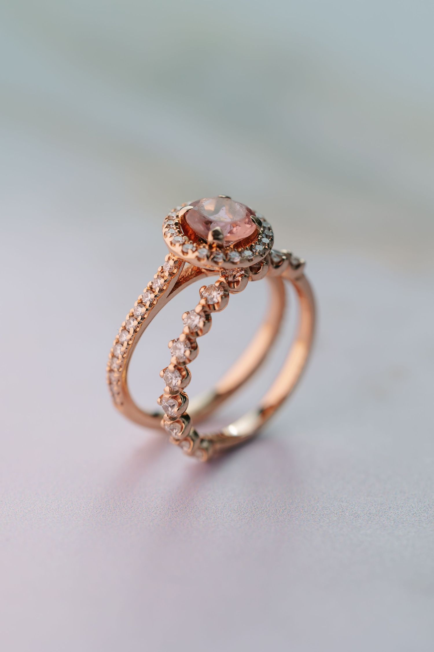 Elegant rose gold halo engagement ring with pink center stone and diamond band on soft background.