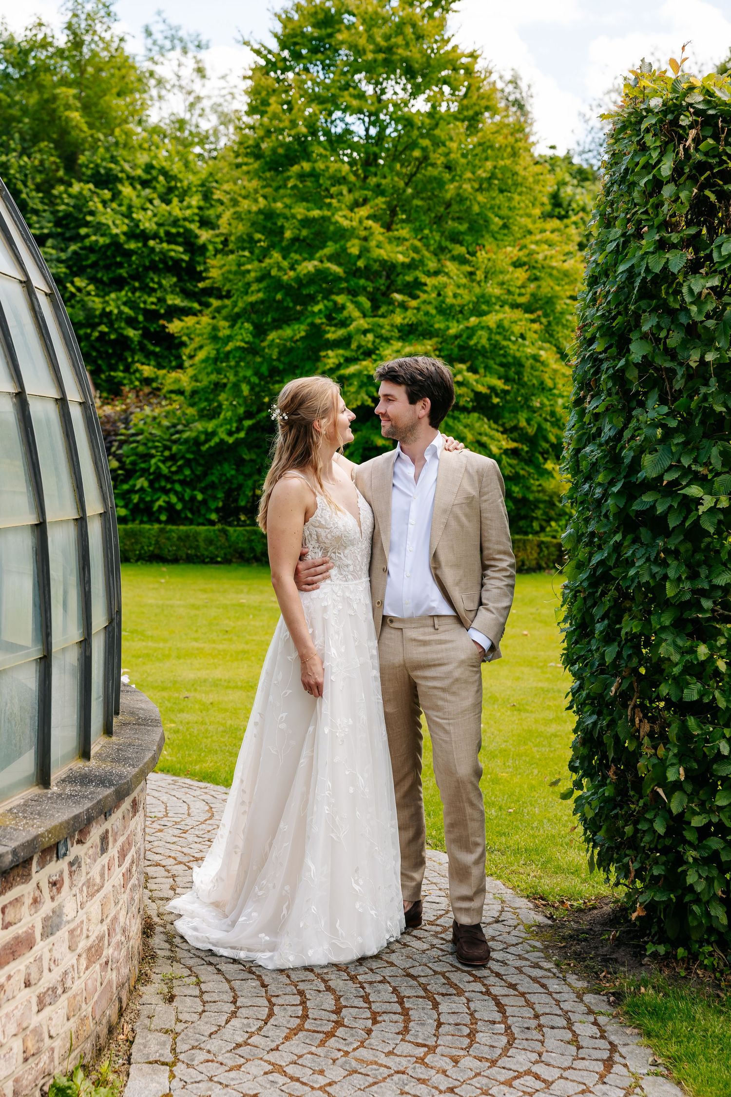 Bride and groom sharing a romantic moment on cobblestone garden path surrounded by lush greenery.
