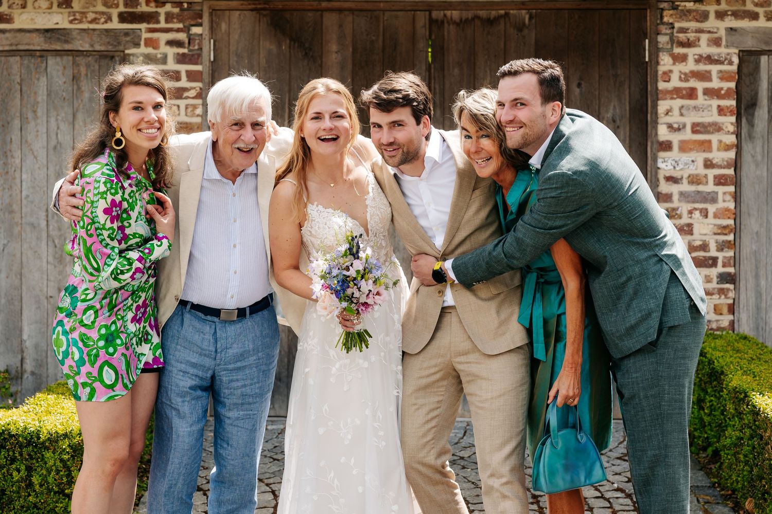 Joyful wedding party of six posing and laughing together outside a rustic brick venue.