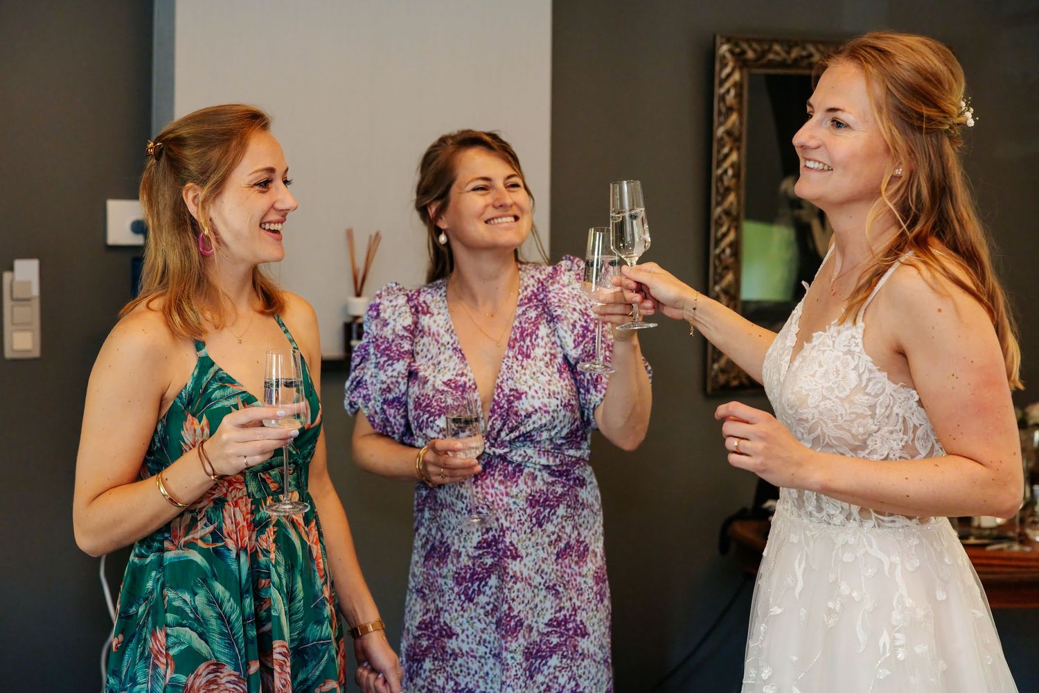 Bride and two bridesmaids toasting with champagne glasses before wedding ceremony.