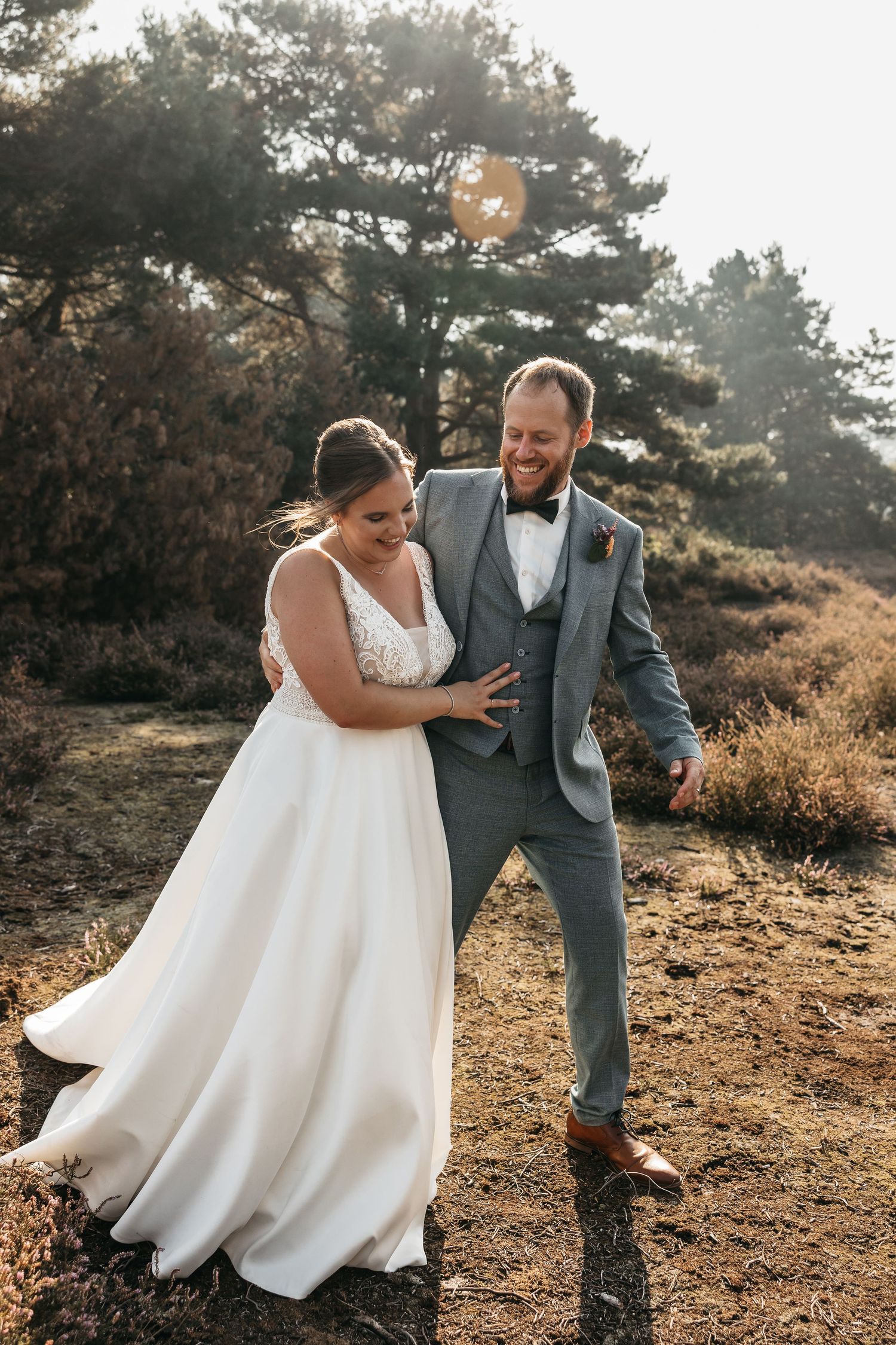 Laughing bride and groom share a playful moment together in a sun-drenched heathland wedding photo.