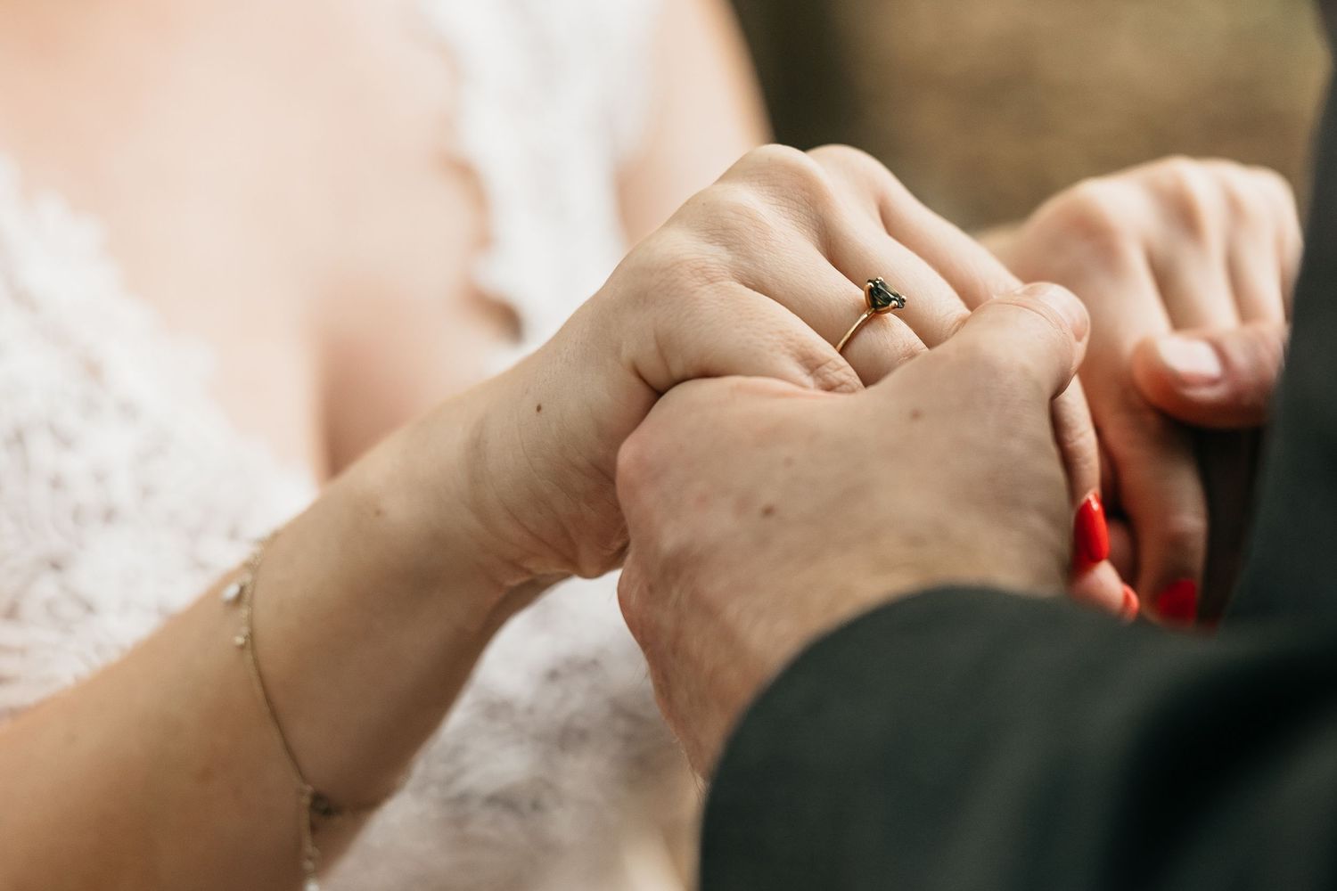 Close-up of bride and groom holding hands with gold wedding ring on wedding day.