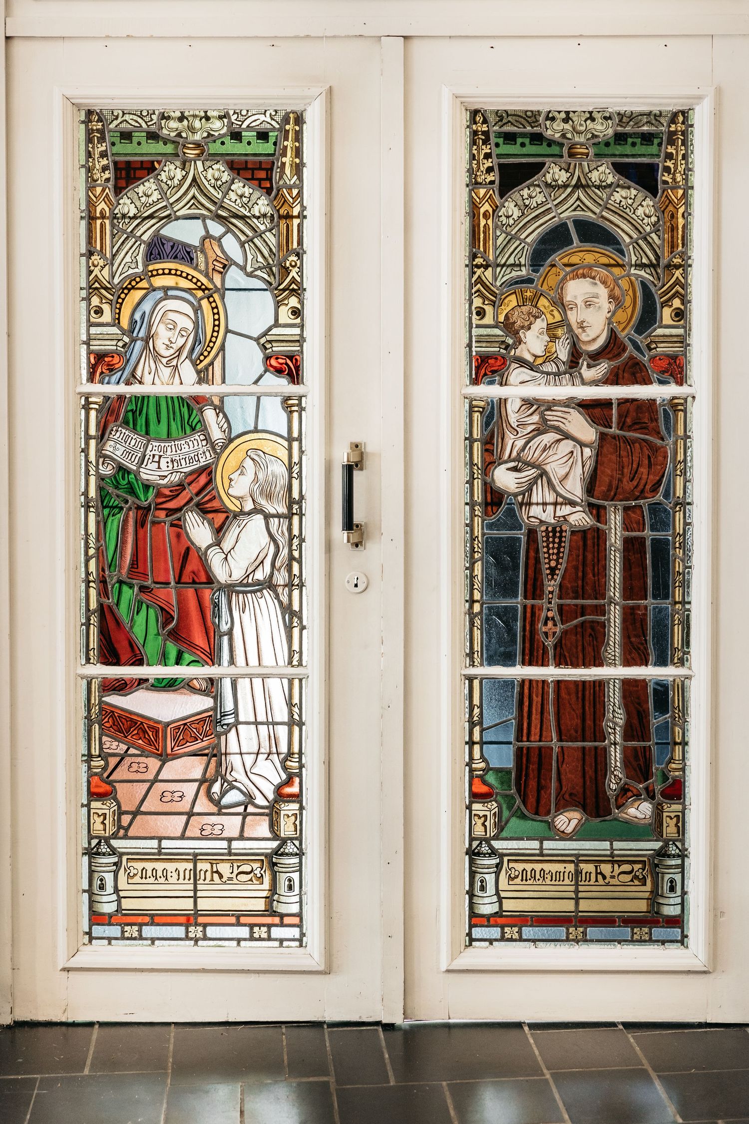Ornate stained glass church doors depicting religious figures including a saint holding the Christ child.